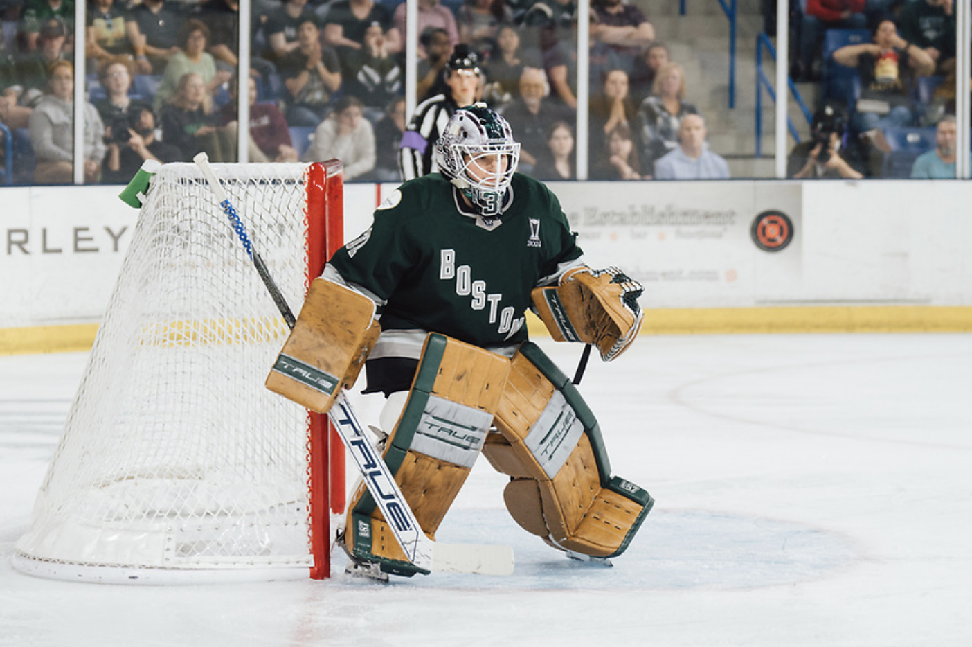Aerin Frankel stands in her crease, slightly crouched while tracking the puck. She is wearing a green home uniform and her tan pads.