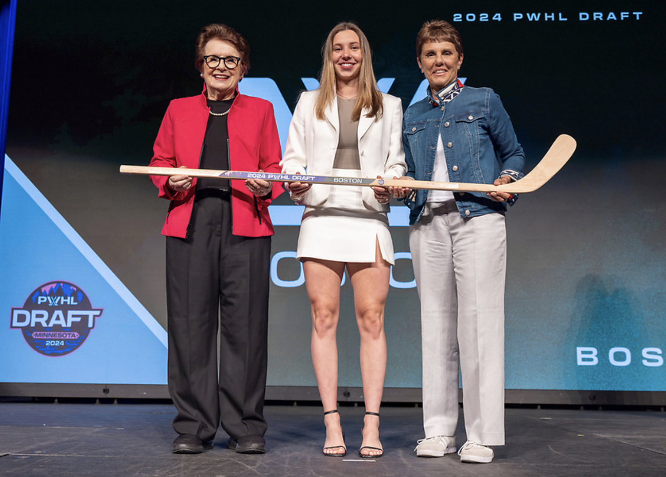 From left to right, King, Bilka, and Kloss pose on stage while holding a wooden PWHL Boston draft stick.