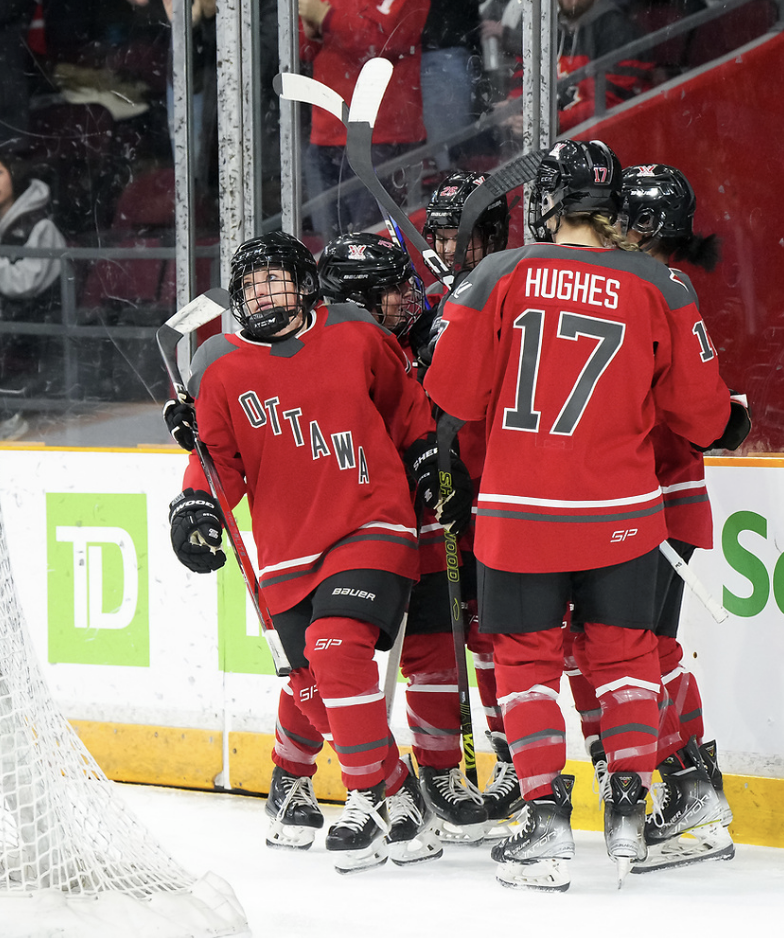 Five Ottawa players celebrate a goal with a group hug. One is starting to skate away to go to the bench. They are all wearing red home uniforms.