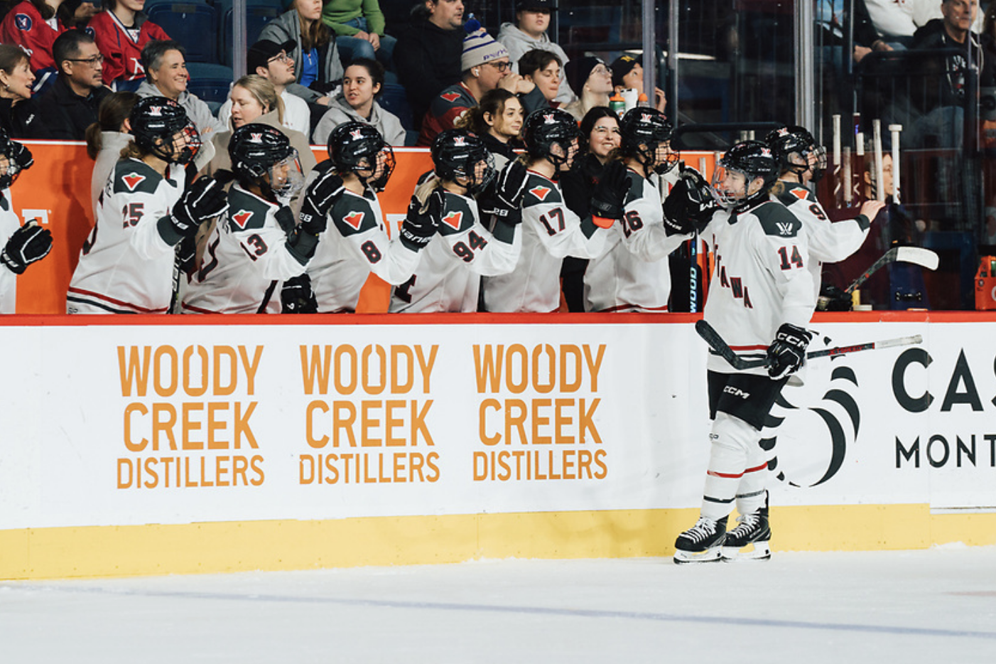 Scamurra skates down the bench to get fist bumps from her teammates after a goal. They are all wearing white away uniforms.