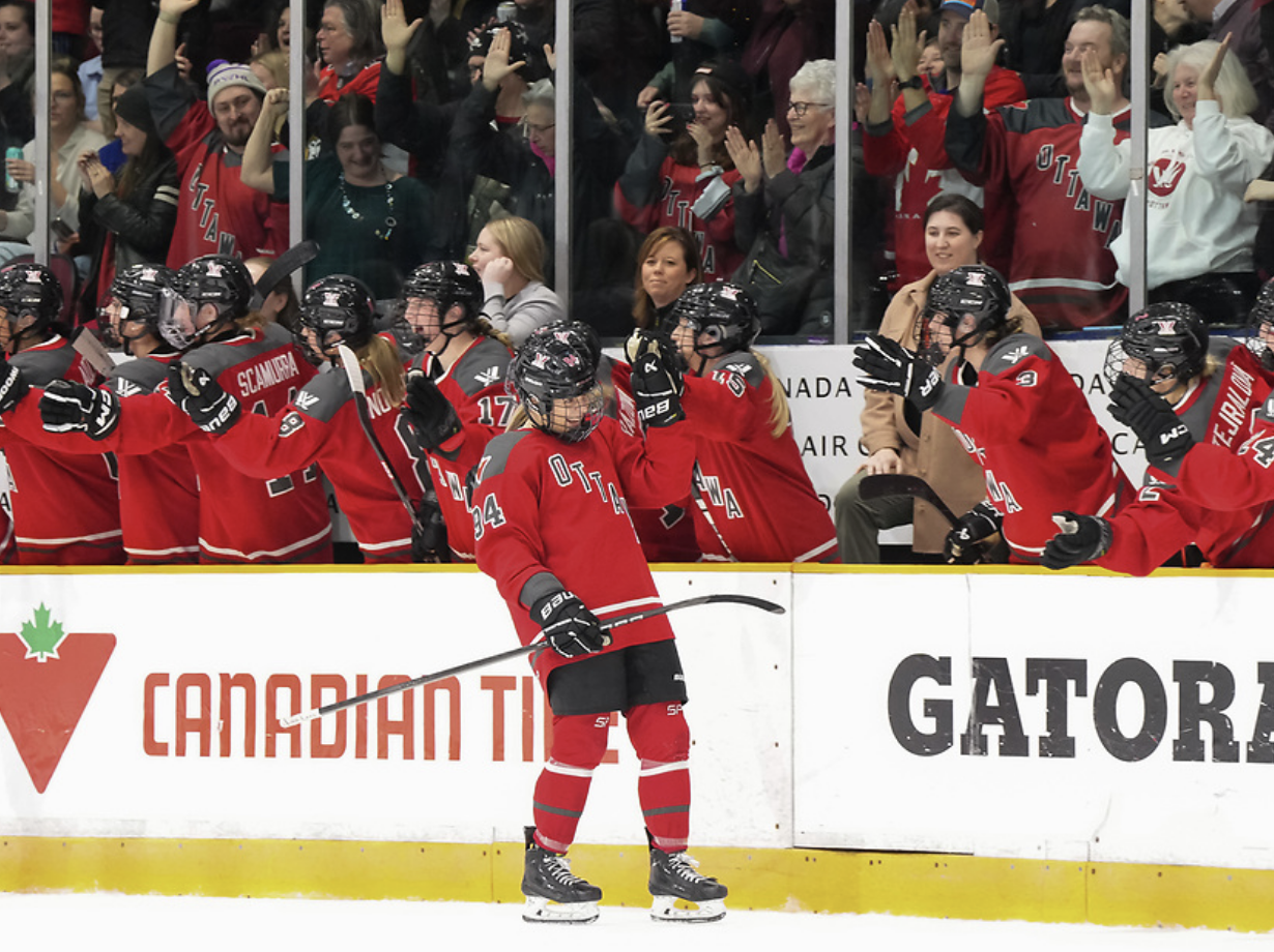 Garát-Gasparics skates down the bench getting fist bumps from her teammates. She is wearing a red home uniform.