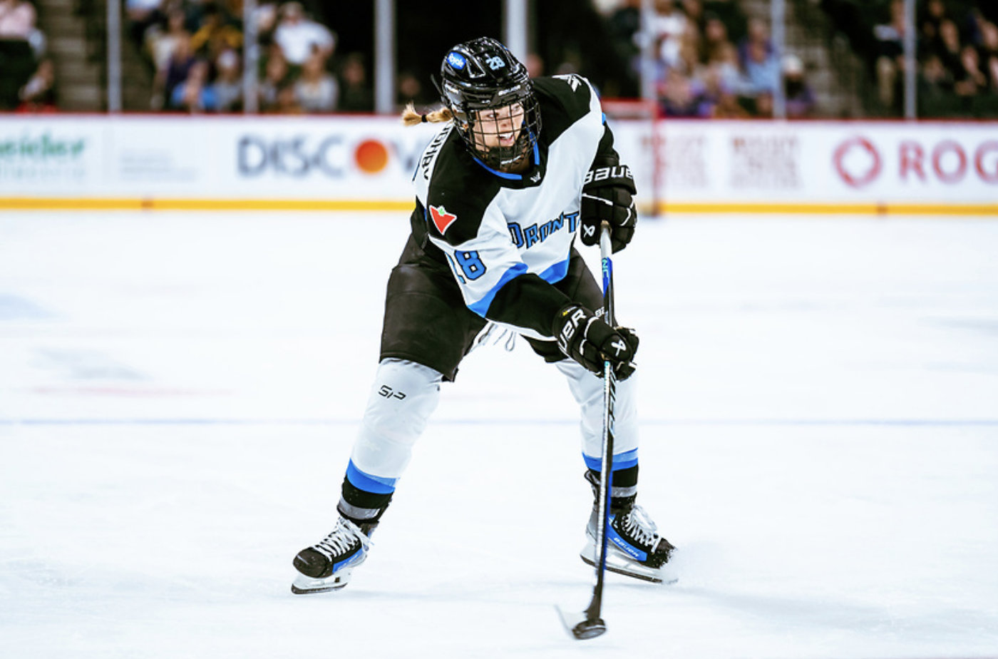 Willoughby skates with the puck just inside the blue line. She is wearing a white away uniform.