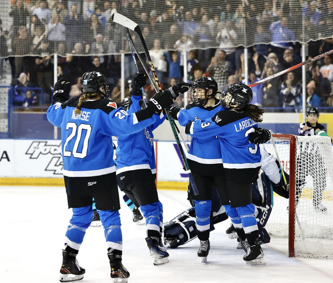 Four Toronto players celebrate a goal against New York with a group hug. They are all wearing blue home jerseys.