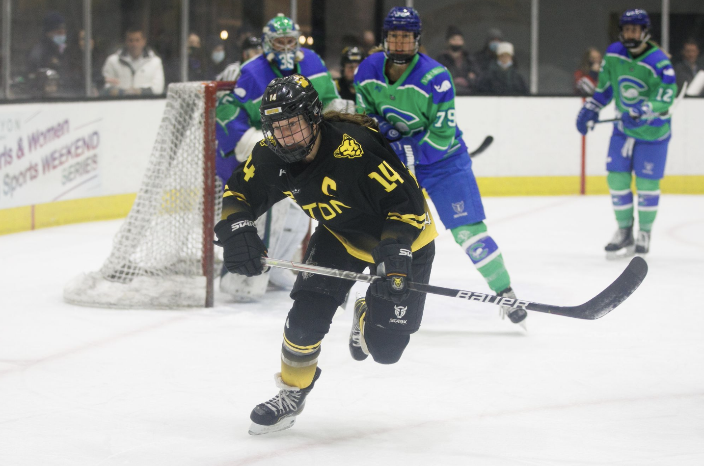 Dempsey skates after a puck in the corner while wearing a black and yellow Boston Pride jersey during a PHF game.