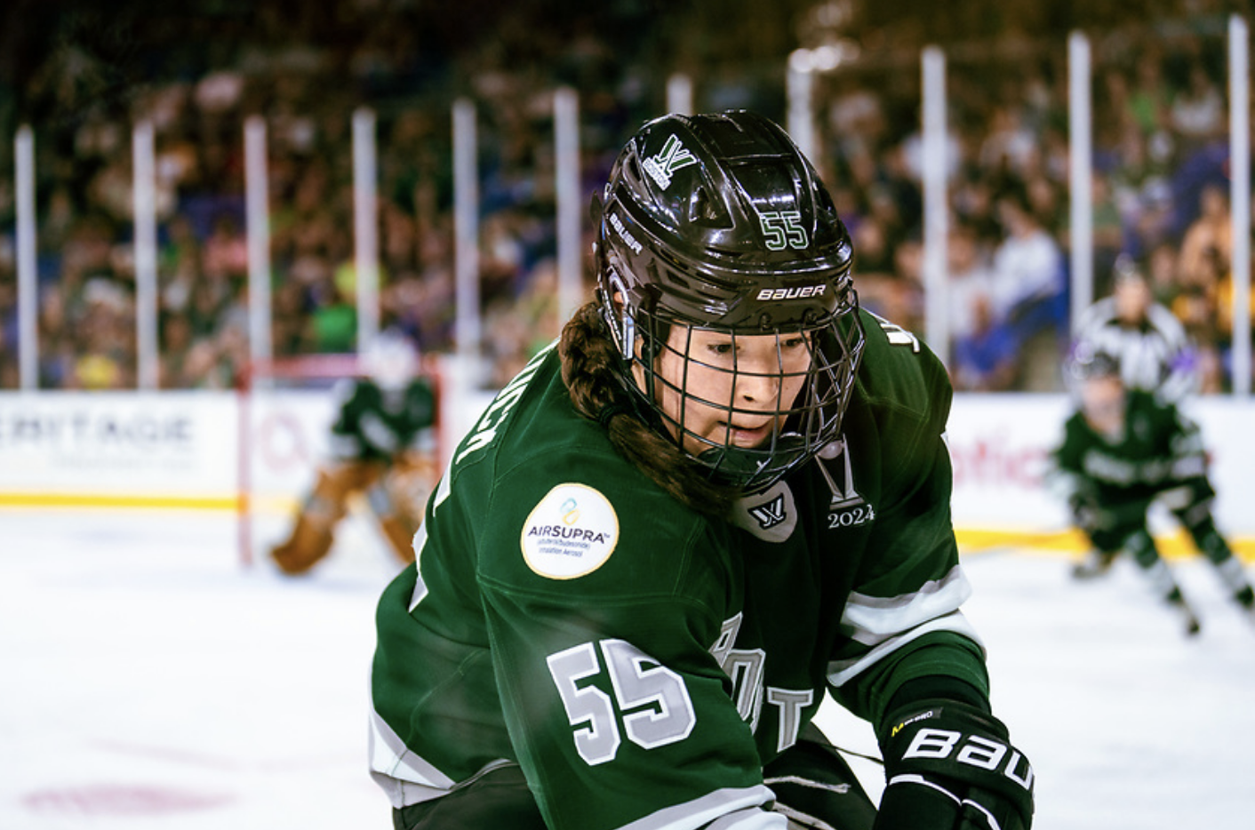 Babstock goes to play the puck during a game. She is looking down at the puck and wearing a green home jersey. 