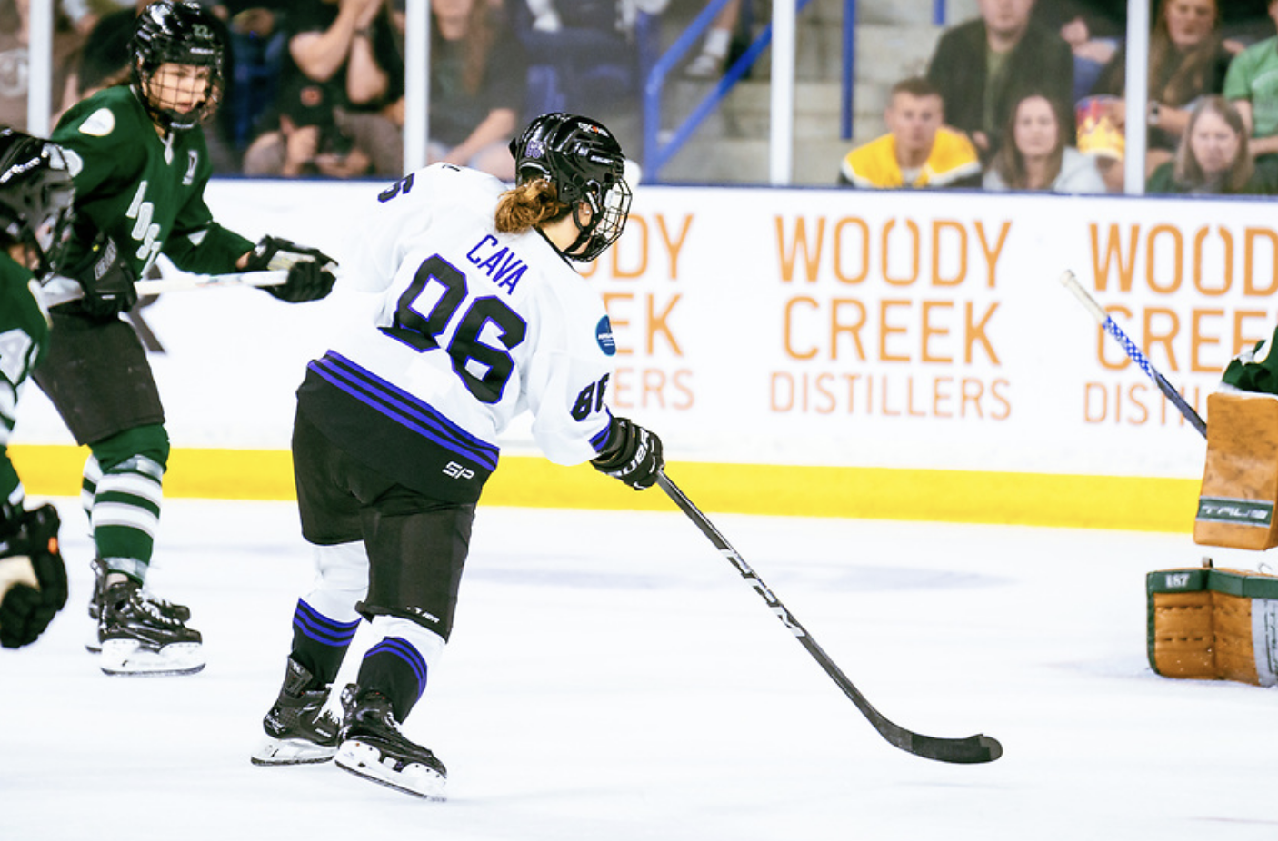 Cava, with her back to the camera, takes a shot on goal. She is wearing a white away uniform.