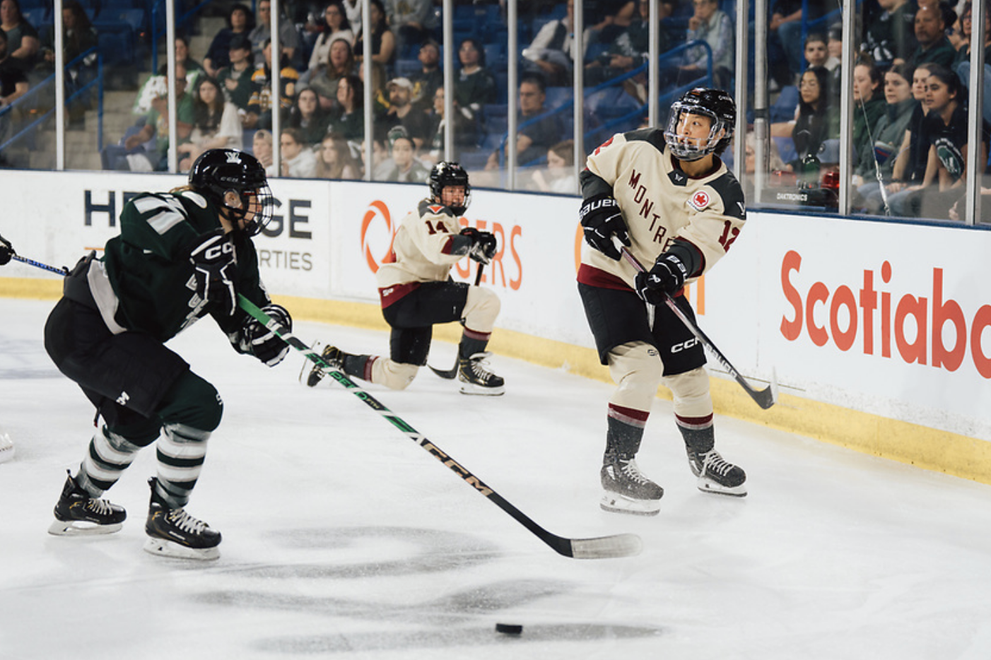 Lum looks up ice after passing the puck while wearing a cream away jersey. A Boston defender is closing in on her.