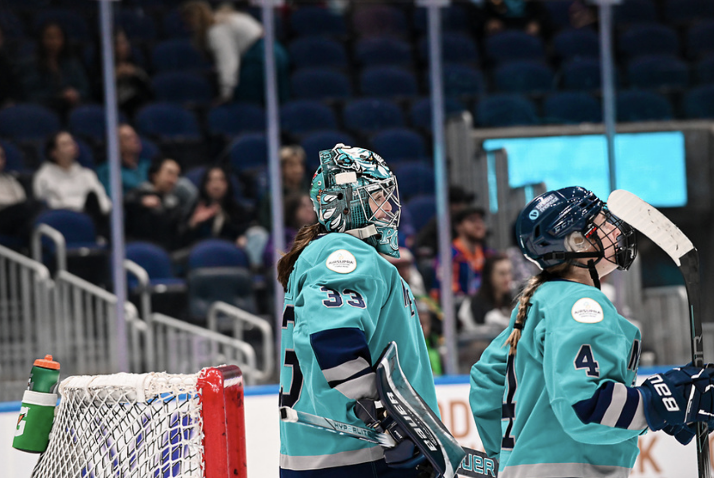 A waist-up shot of Post and Baker standing in front of Post's net and looking up ice. They are wearing teal home uniforms.