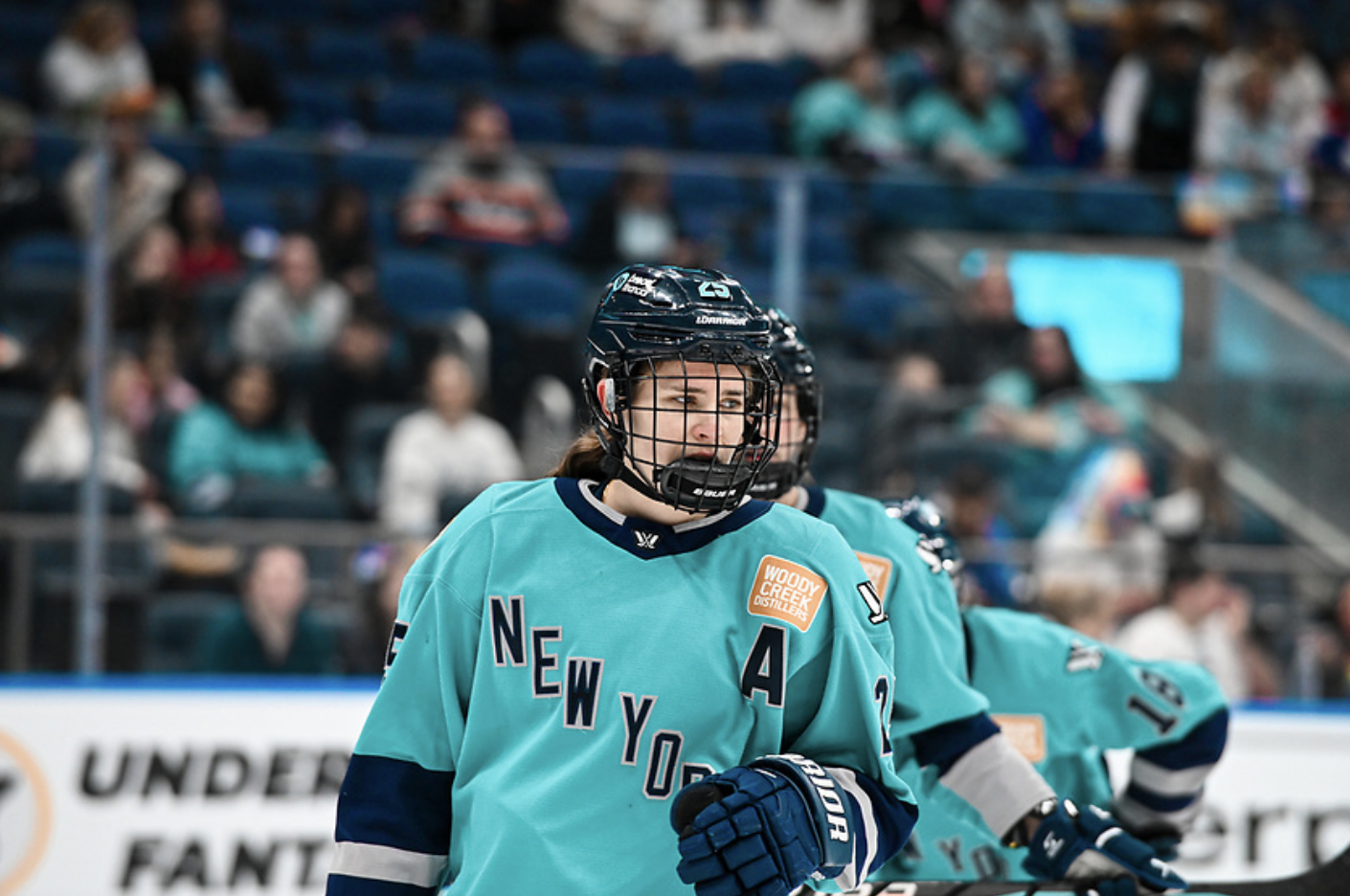 A waist-up shot of Carpenter preparing for a face-off. She is wearing a teal home jersey.