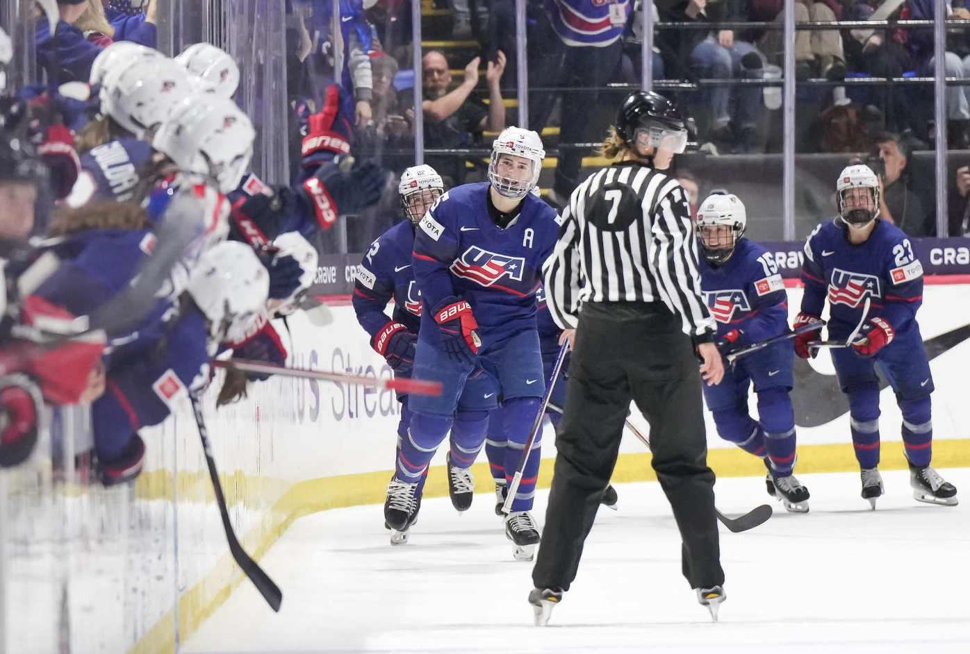 Megan Keller and four teammates face the camera as they skate towards to celebrate a goal. They are all wearing blue uniforms.