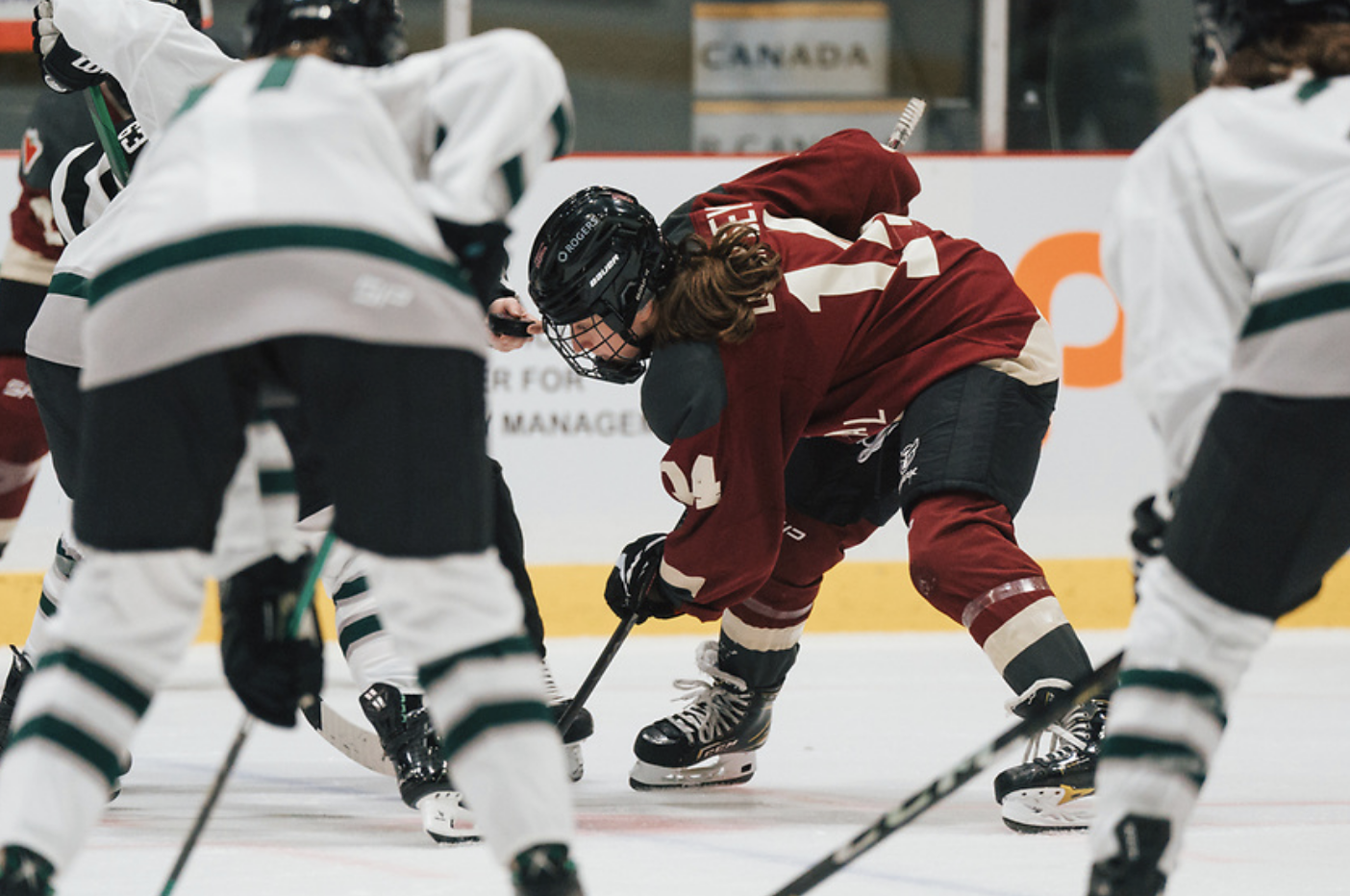 Dempsey is bent over with her stick in the face-off circle, look at the puck in the referee's hand. She is wearing a maroon Montréal jersey.