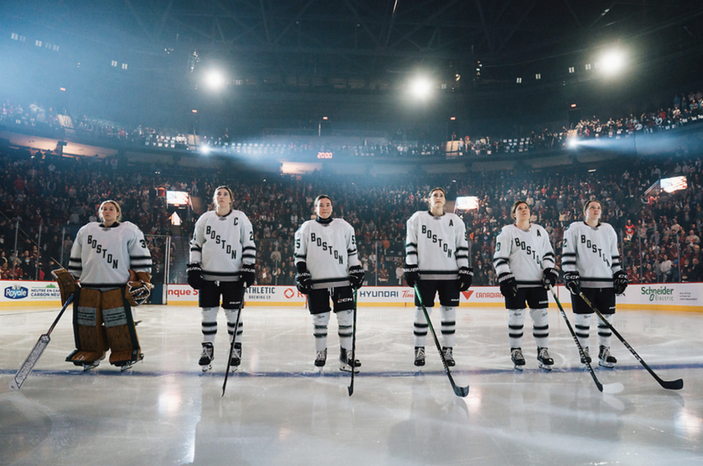 In their white uniforms, five Boston players stare ahead while standing along the blue line.