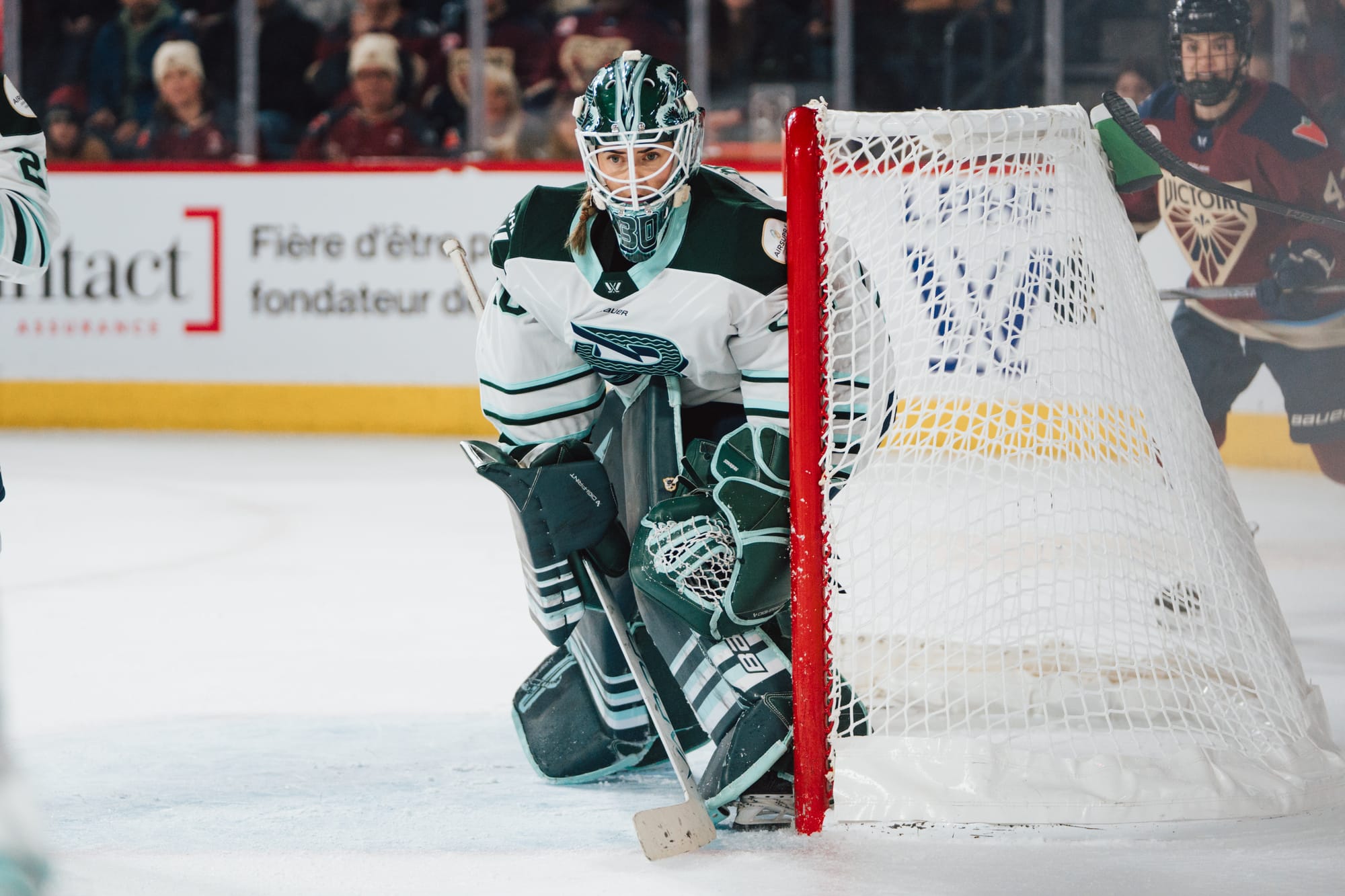 From her net, Söderberg looks to her left and watches a play develop. She is crouched as she tries to seal all gaps. She is wearing a white away uniform and her green pads and mask.