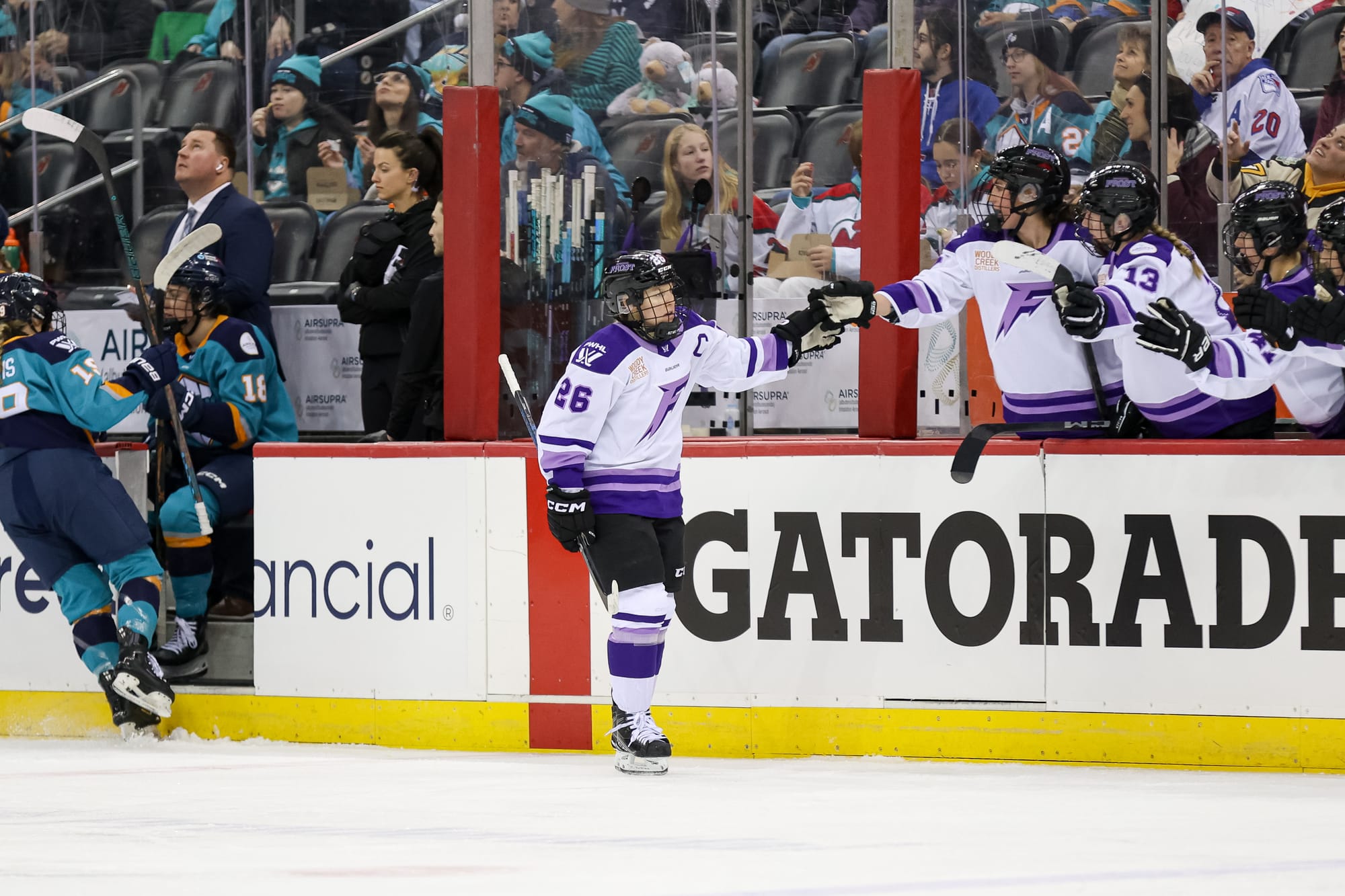 A side view of Coyne Schofield celebrating a goal by going down the handshake line at the bench. She is wearing a white away uniform. 