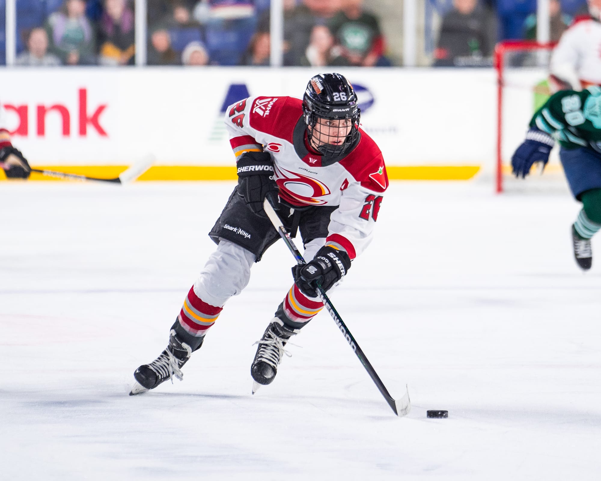 Clark is leaning forward and looking up. She is skating with her stick and the puck in front of her and wearing a white away uniform. 