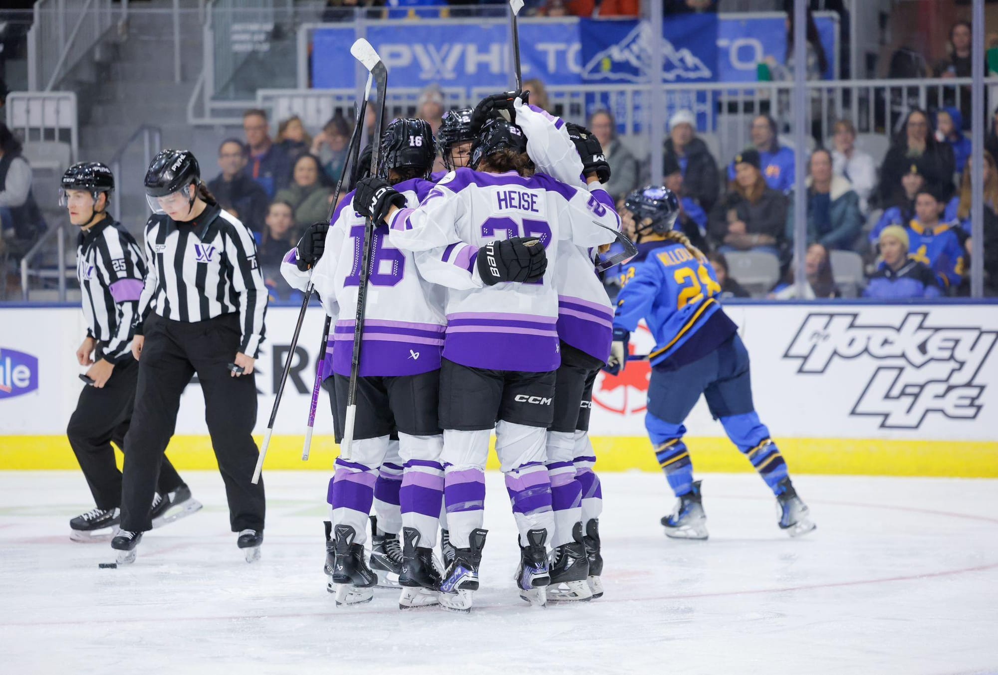 Five Minnesota skaters celebrate a goal with a tight group hug. They are wearing white away jerseys.