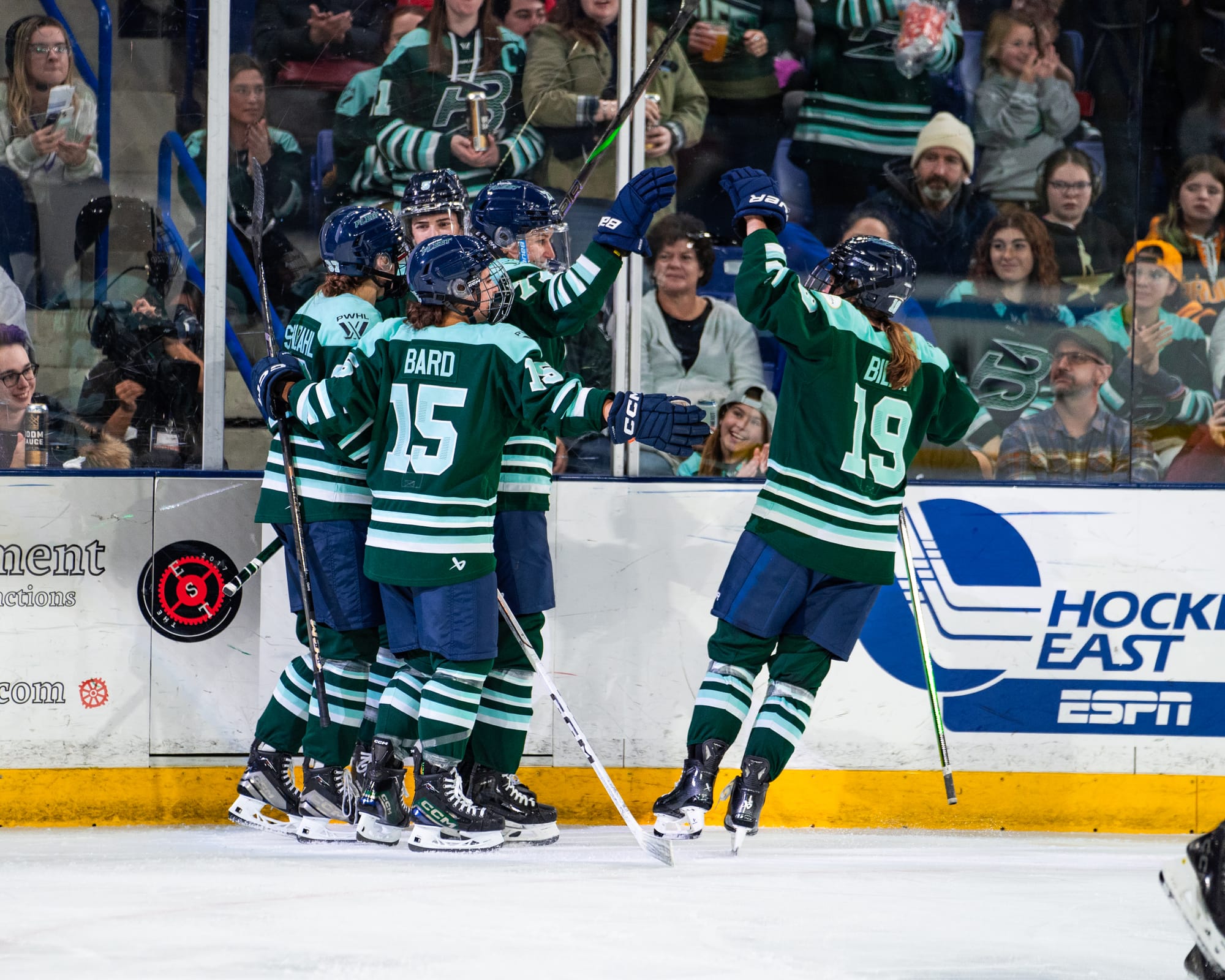 Four Fleet players are already in the celebratory group hug, while Hannah Bilka is skating in to join. They are all wearing green home uniforms.