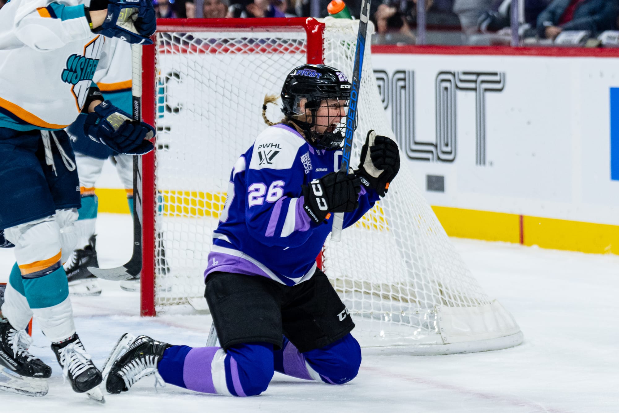 Coyne Schofield is kneeling right by the side of the net, pumping her fists and yelling in celebration. She is wearing a purple home jersey.