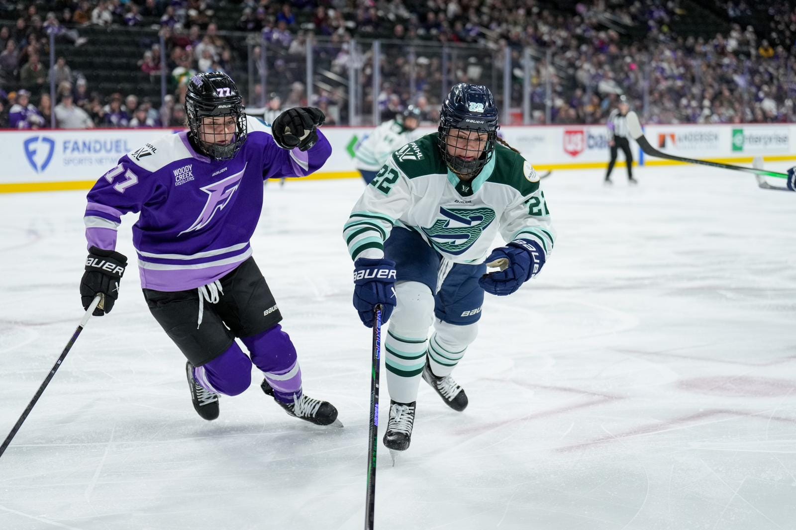 DiGirolamo (right in white) looks down and ahead at the puck (which is out of frame) as she makes a play against Curl-Salemme (left in purple), who is also watching the puck.