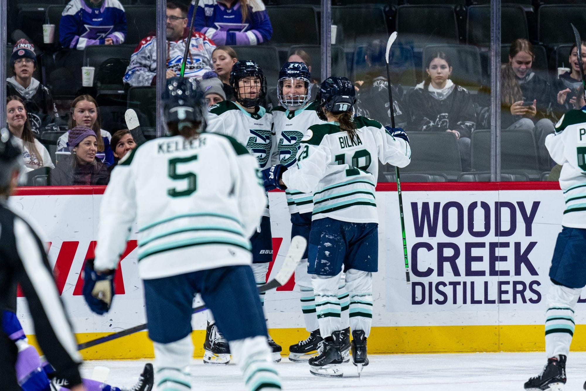 Three Boston players celebrate a goal with a group hug. Two others are skating to join. They are wearing white away uniforms.