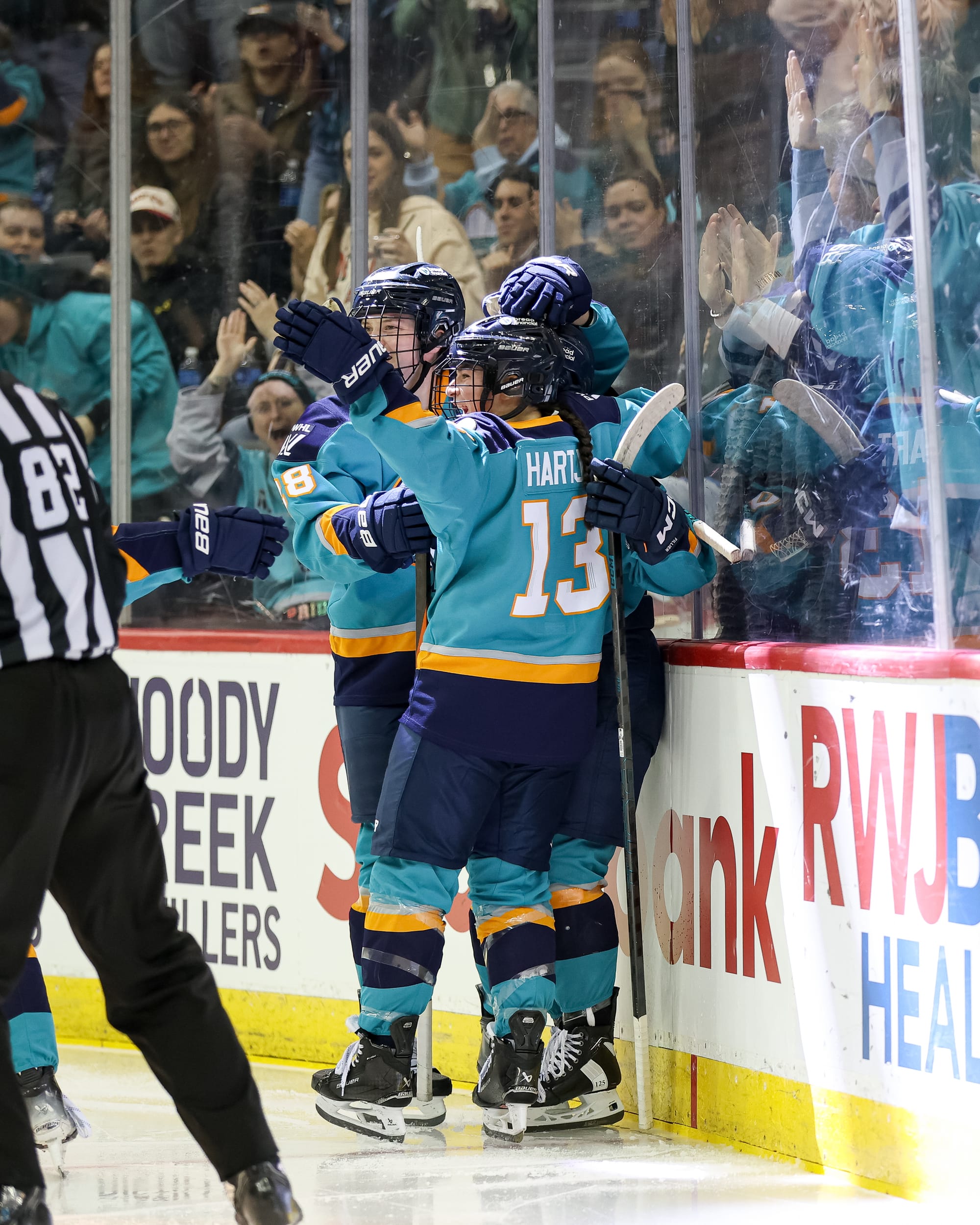 Sirens players celebrate a goal with a group hug. They are wearing teal home uniforms.