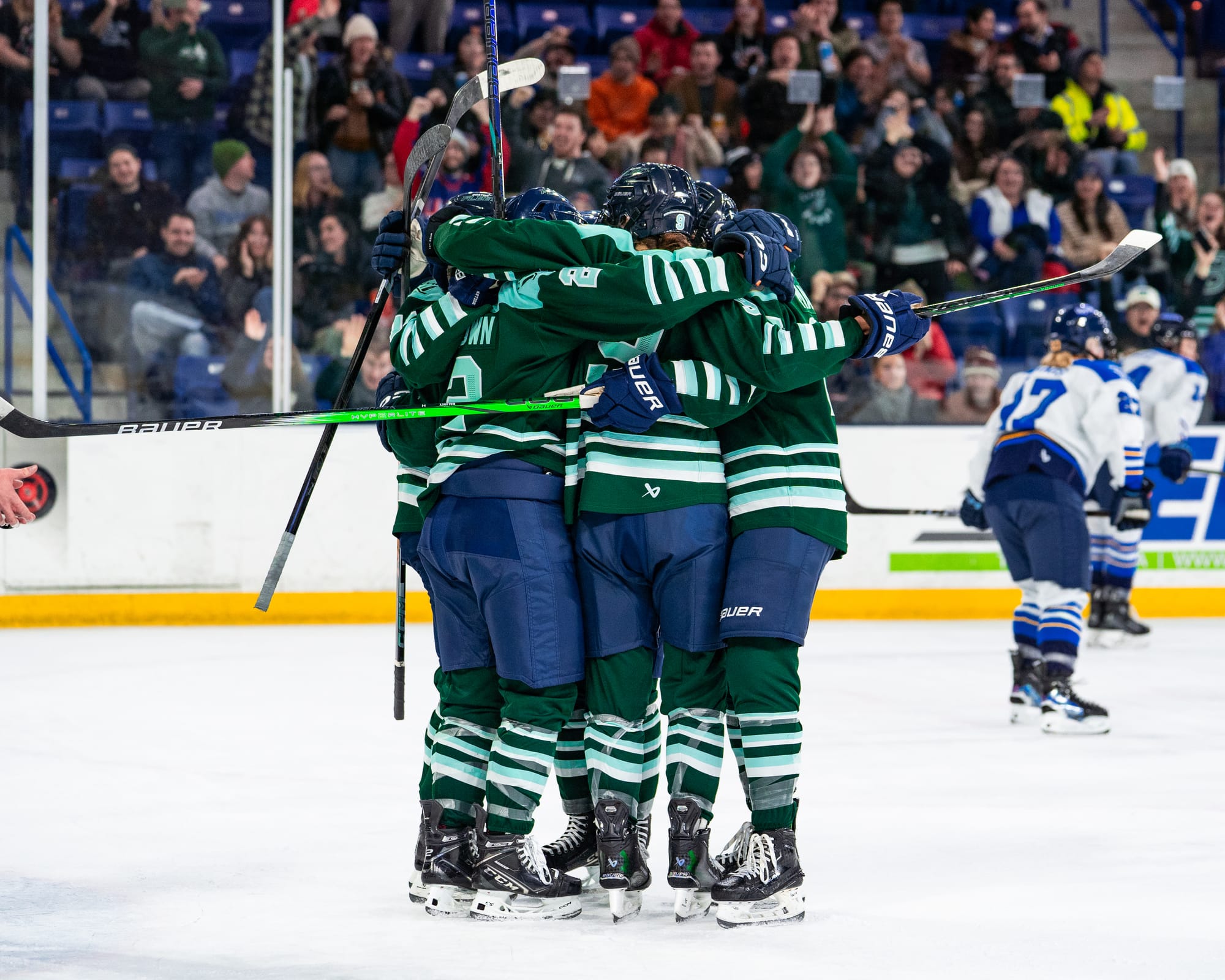 Five Fleet players celebrate a goal with a tight group hug. None are facing the camera, and they are wearing green home uniforms.