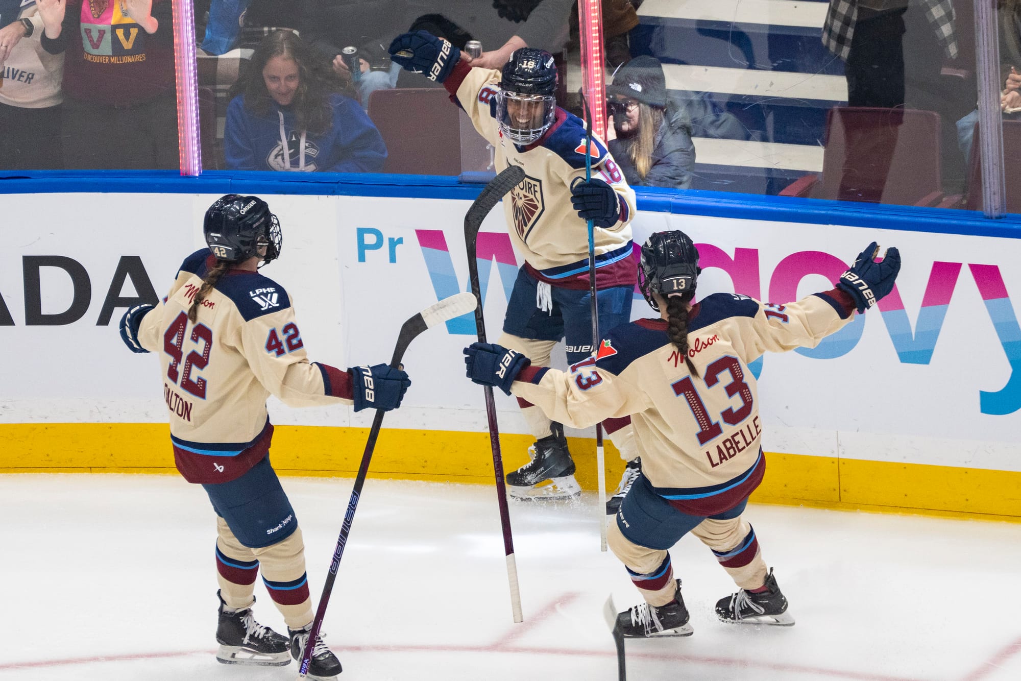 Three Victoire players have their arms wide open and are about to enter a group hug to celebrate a goal. Two have their backs turned toward the camera while another faces the camera. They are wearing cream away uniforms.