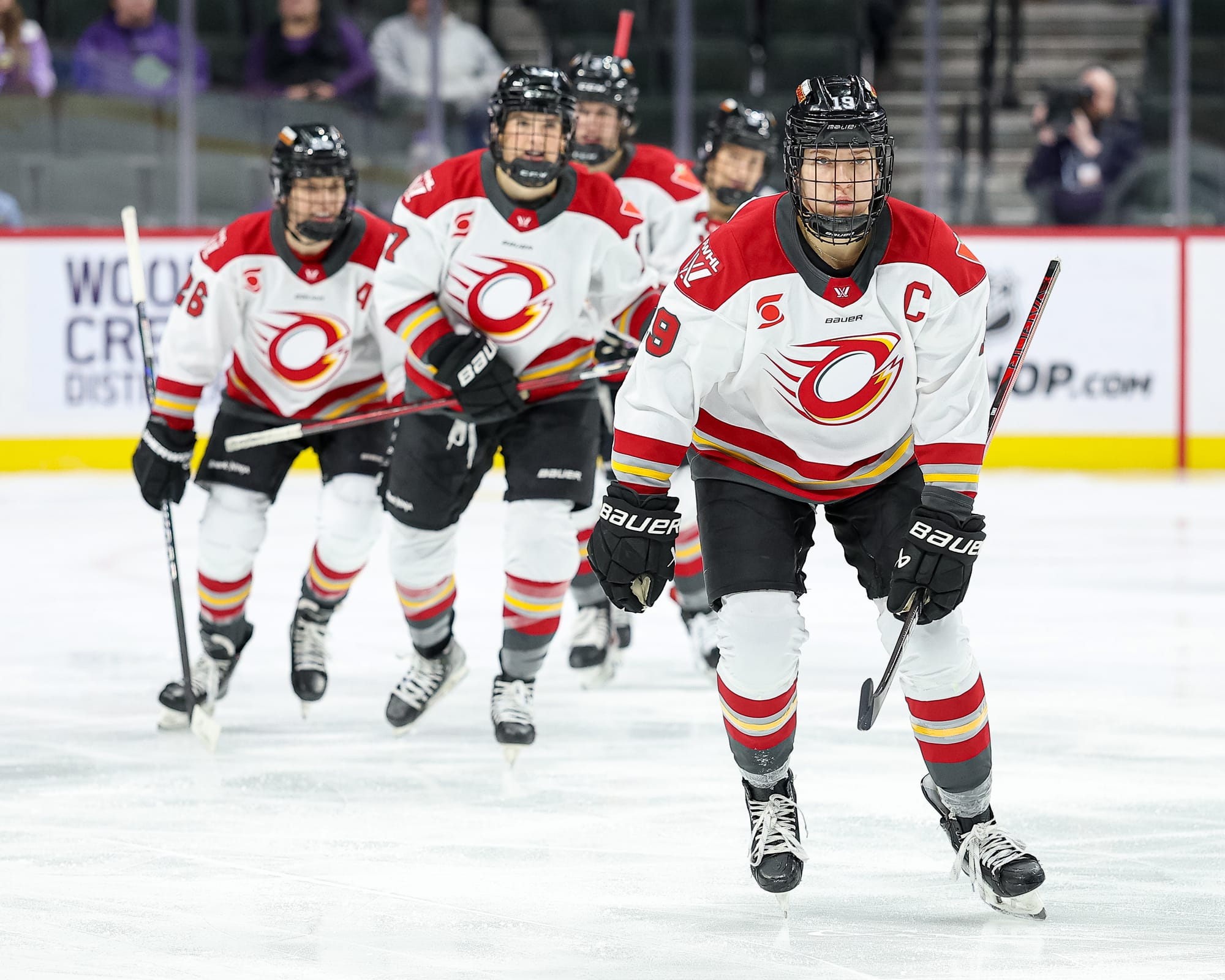 Five Charge players skate in a jagged line towards the bench. They are all facing the camera and wearing white away uniforms.