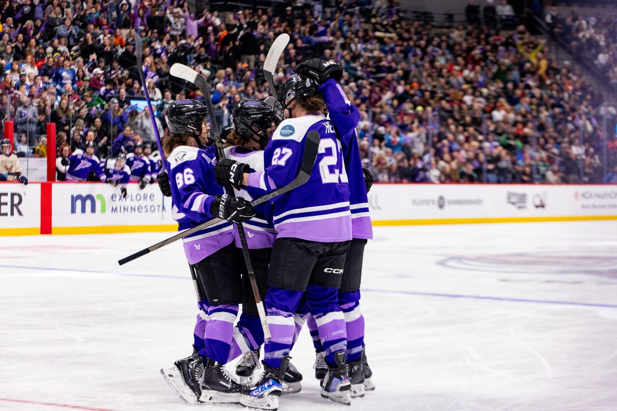 Minnesota players celebrate a goal with a tight group hug just above one of the circles. They are wearing purple home uniforms.