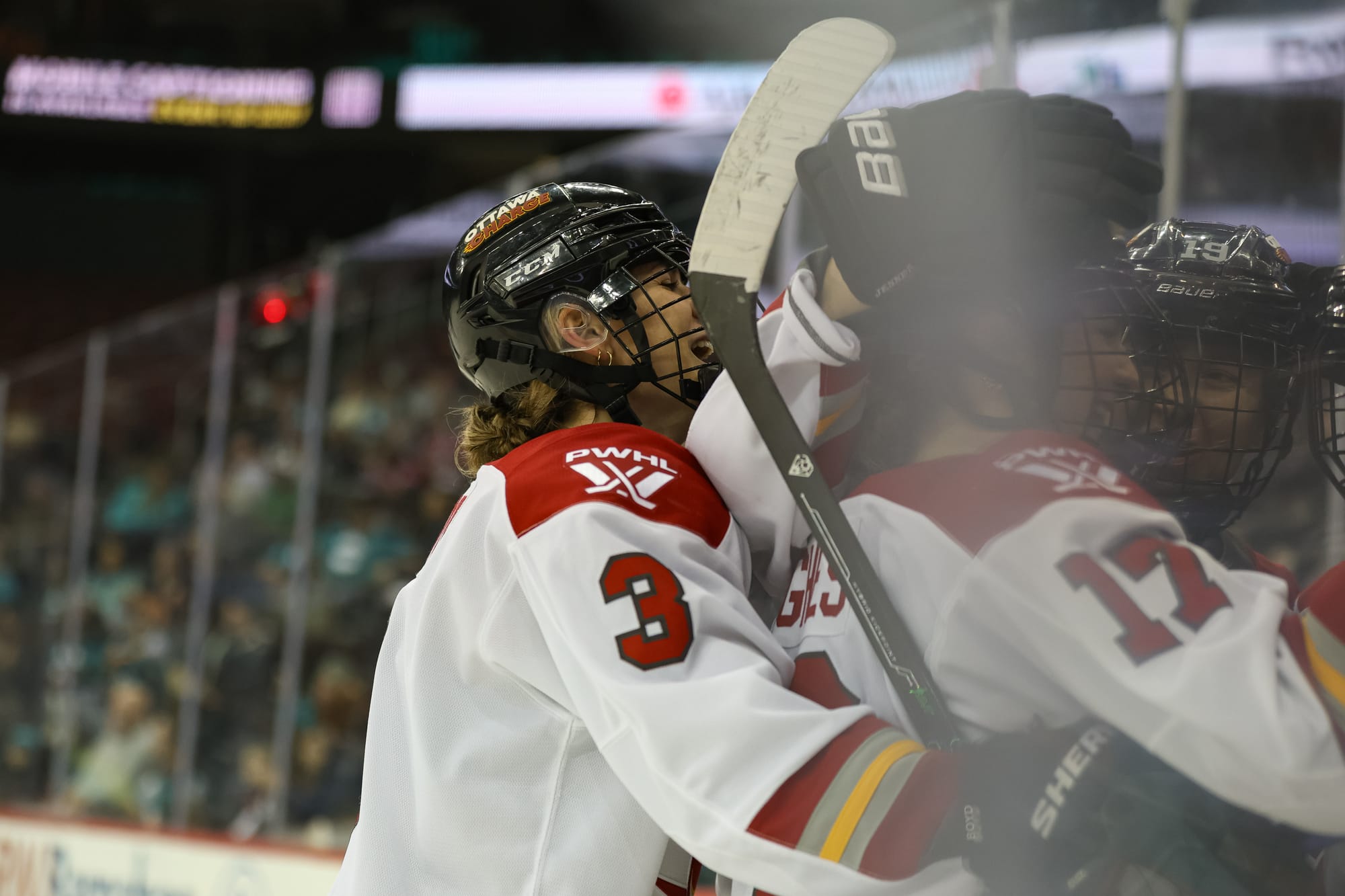 An up-close look at a celebratory Ottawa tight group hug. Three players are in the frame, and they are wearing white away uniforms.