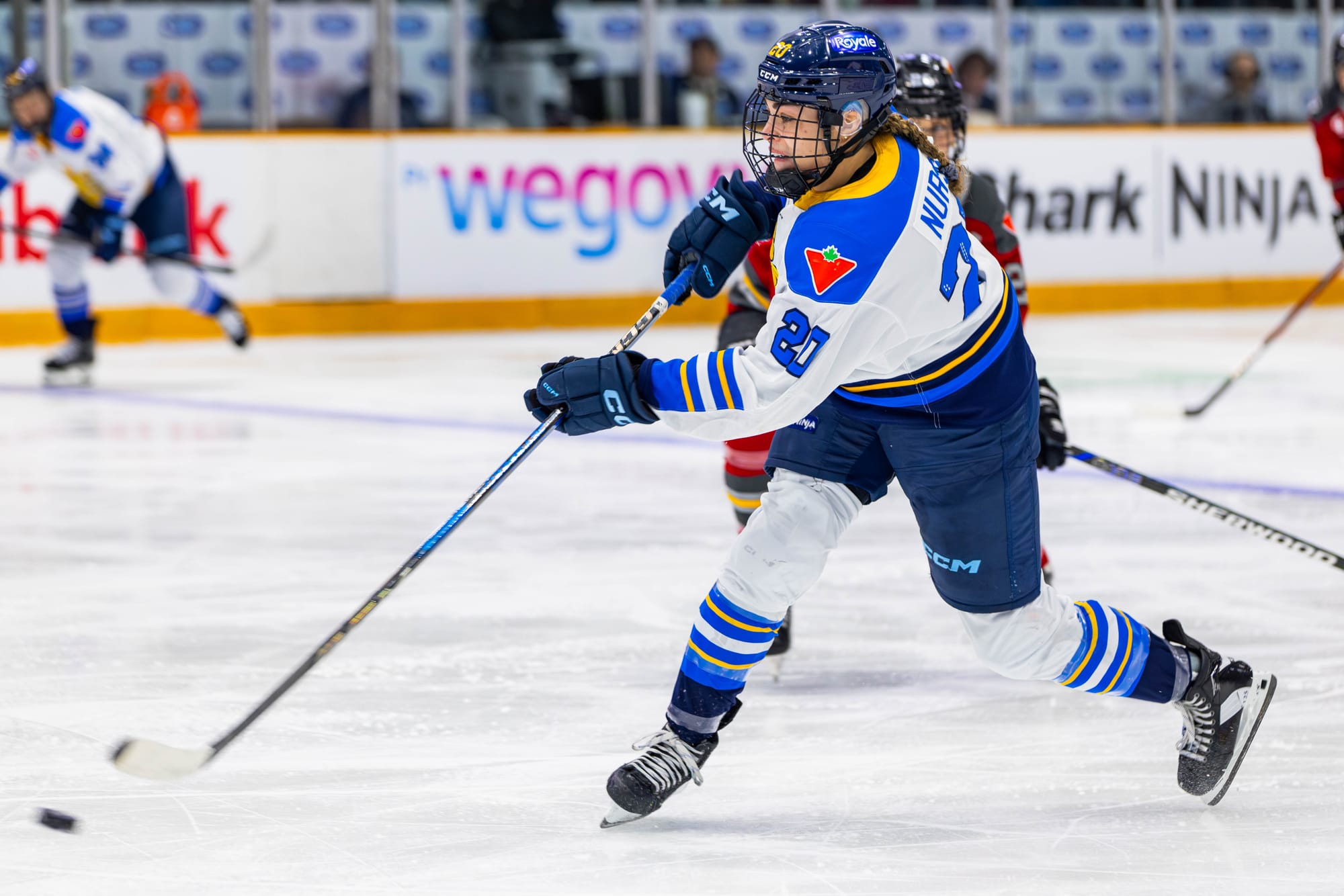 Nurse takes a shot. The puck is just leaving her stick, which is slightly elevated, and most of her weight is on her right left. She is wearing a white away uniform.