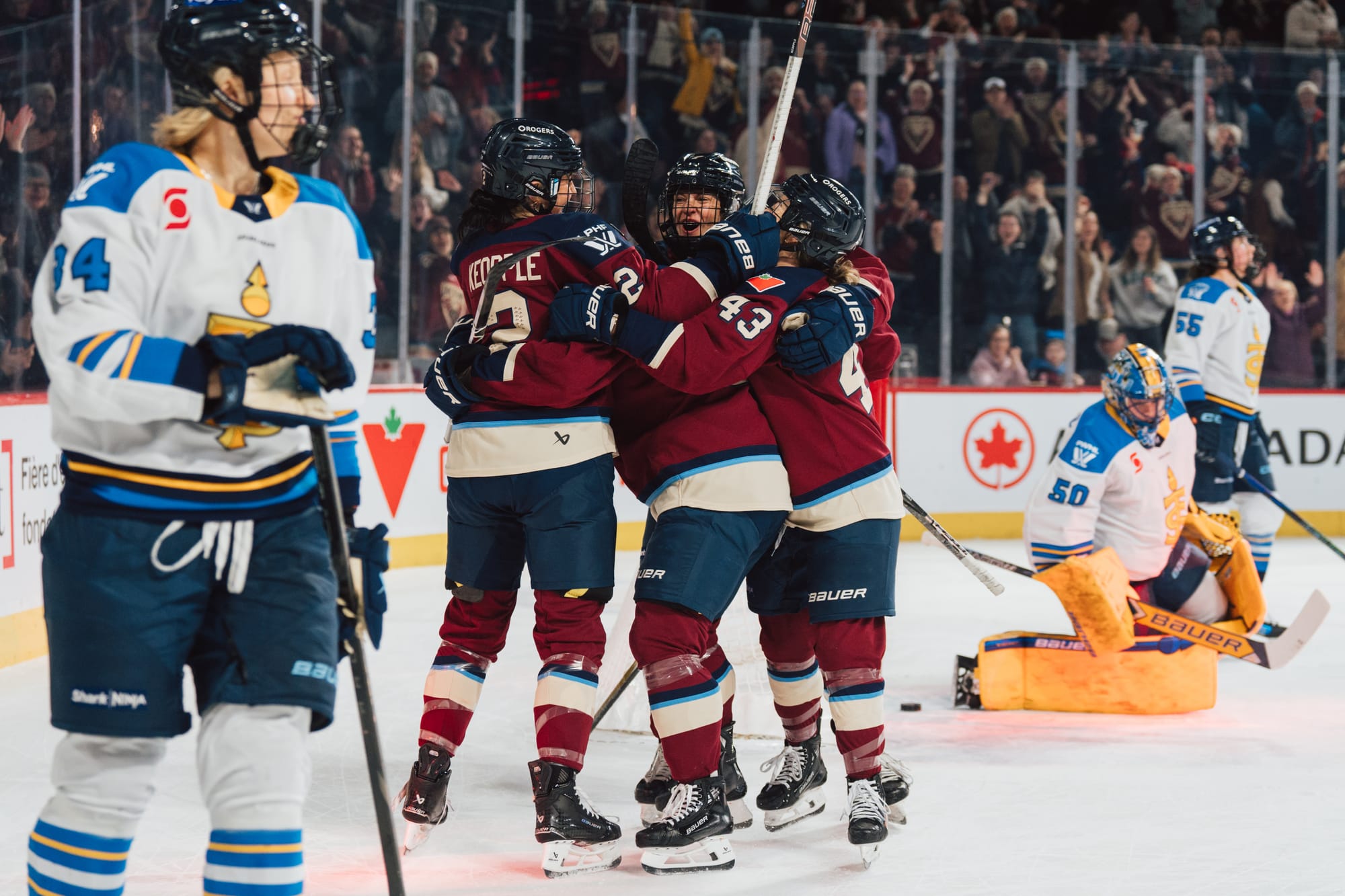 Montréal players celebrate with a tight group hug off to the right of the goal.. They are wearing maroon home uniforms.