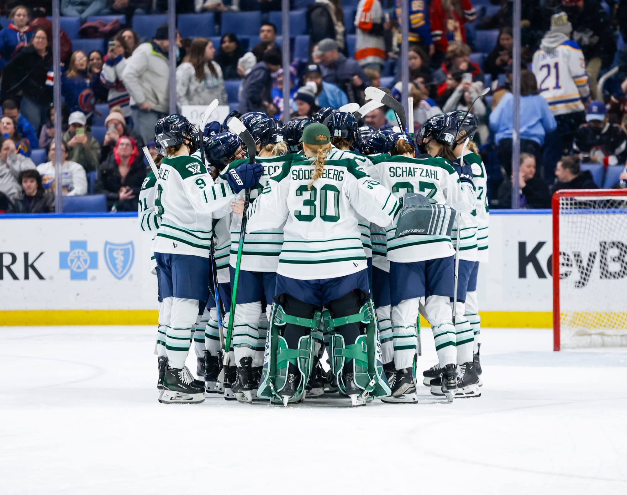 All of the dressed Fleet players are in a tight group hug by one of the nets. No one is facing the camera. They are wearing white away uniforms.