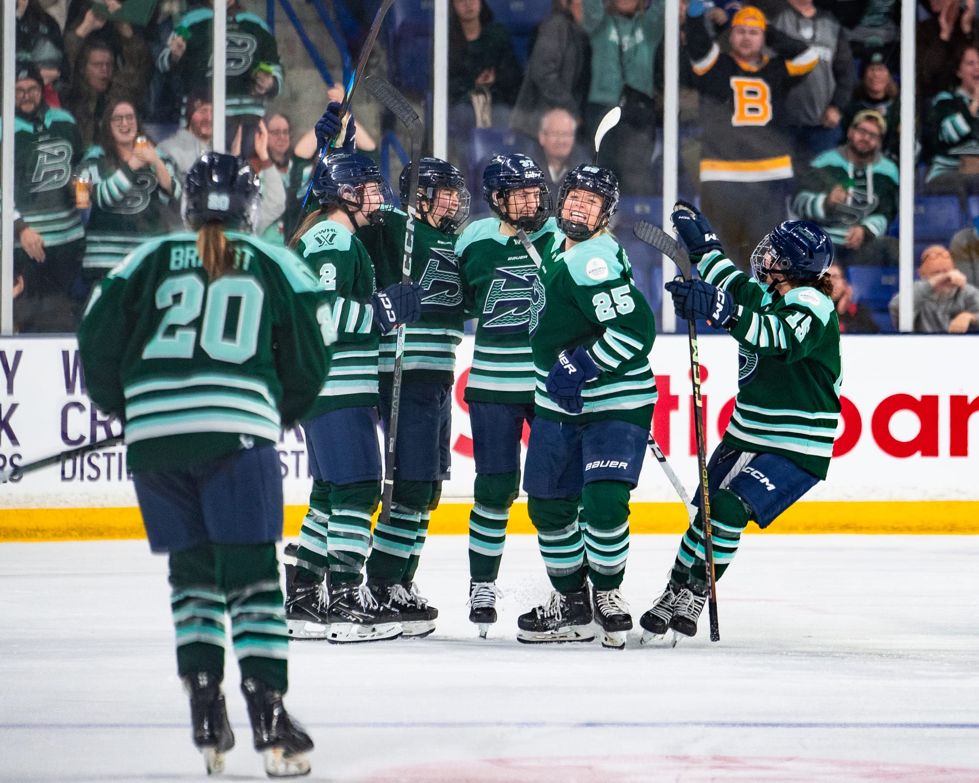 Five Fleet players celebrate with a group hug. Hannah Brandt is also skating to join. They are wearing green home uniforms.