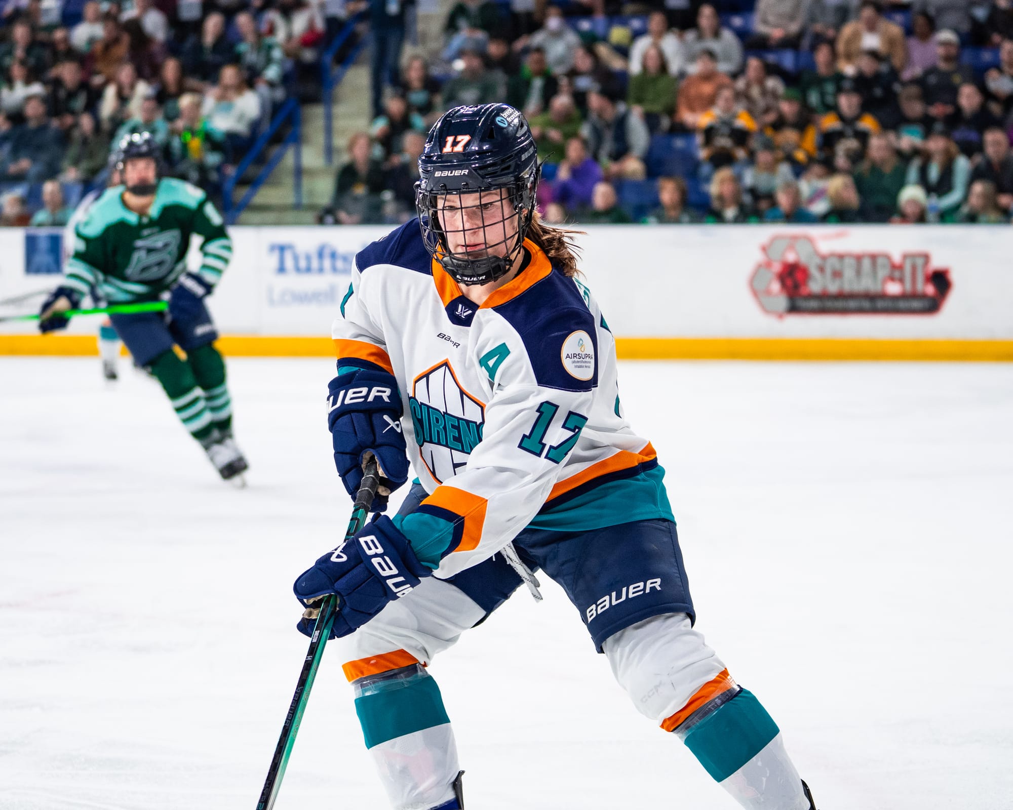 Shelton looks down as she makes a play on the puck (which is out of frame). She is wearing a white away uniform.