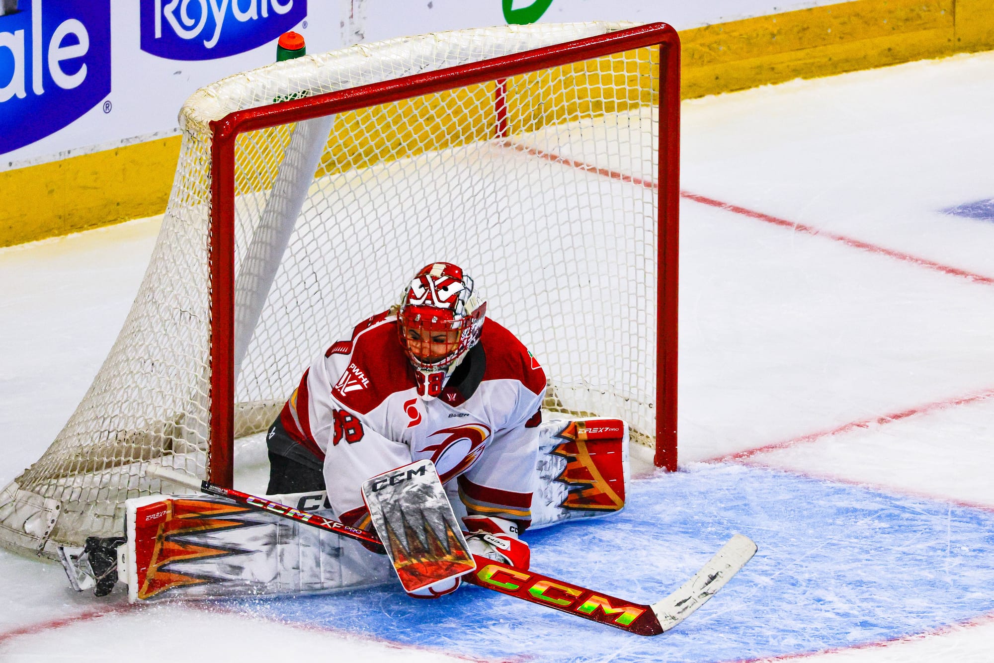 Maschmeyer is on her knees, sliding across the crease. Her right leg is just going past the post. She is wearing a white away uniform.