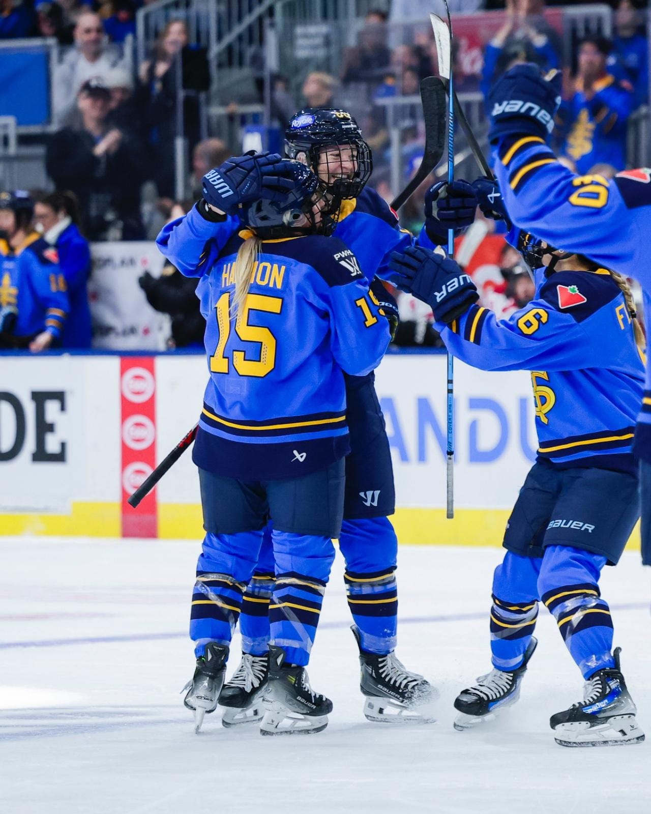 Three Sceptres players celebrate with a group hug near the blue line. They are wearing blue home uniforms.