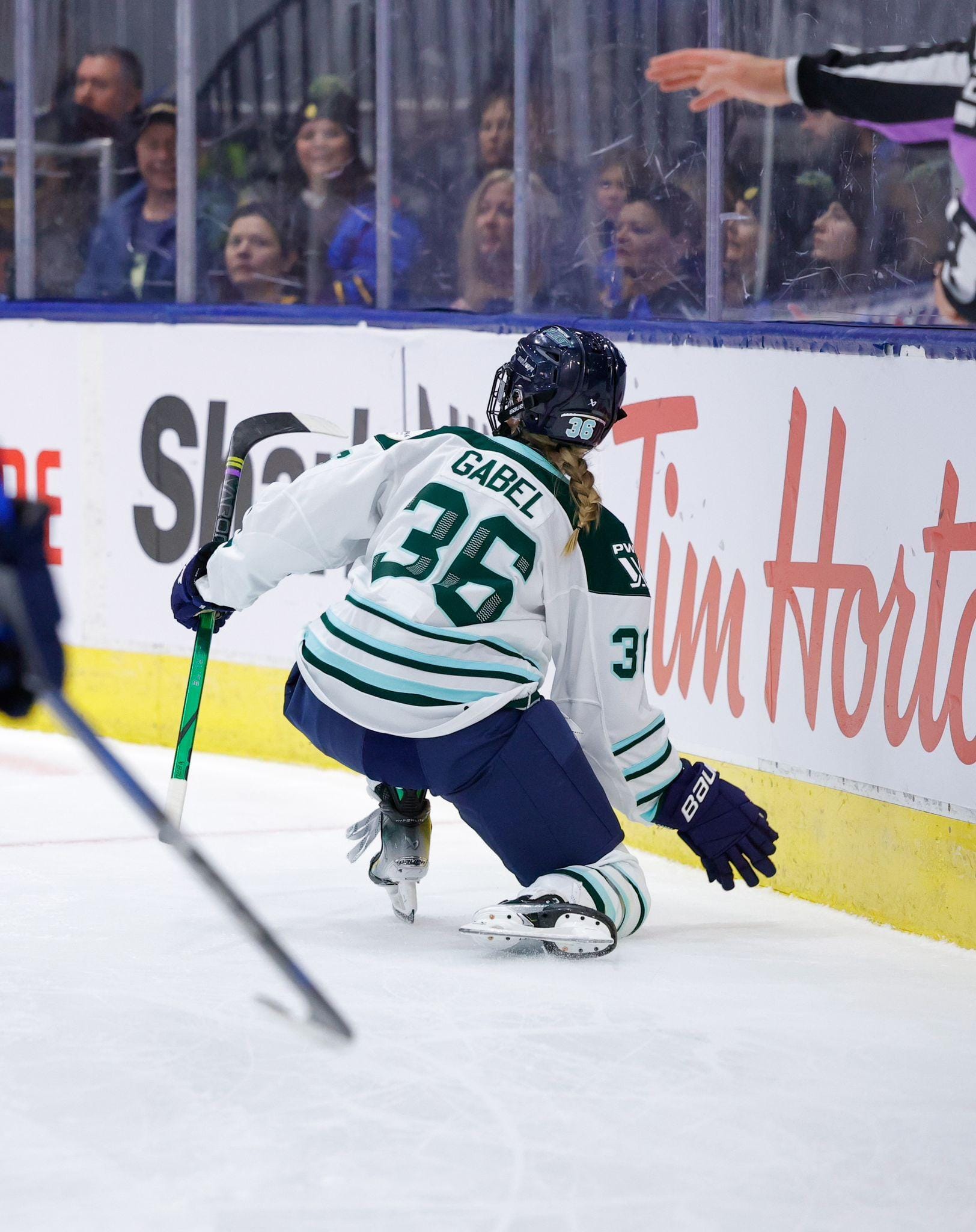 Gabel puts her right knee on the ice as she moves forward, and reaches her right hand down in celebration. She is back to the camera, and wearing a white away uniform.