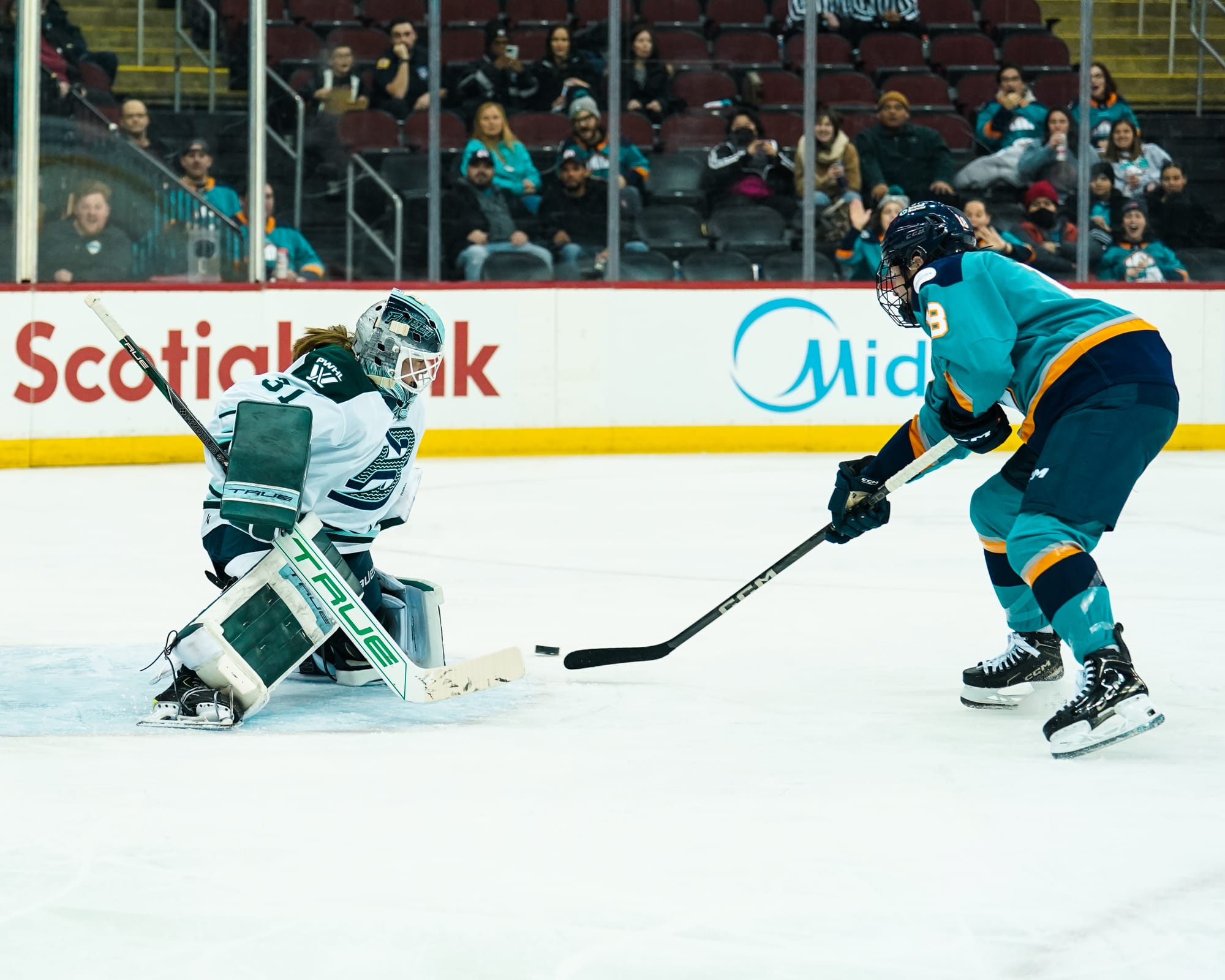 Giguère (right in blue) loses the puck as she approached the top of the crease. Frankel (left in white) is on her knees at the top of the crease, pushing to her left to track the puck.