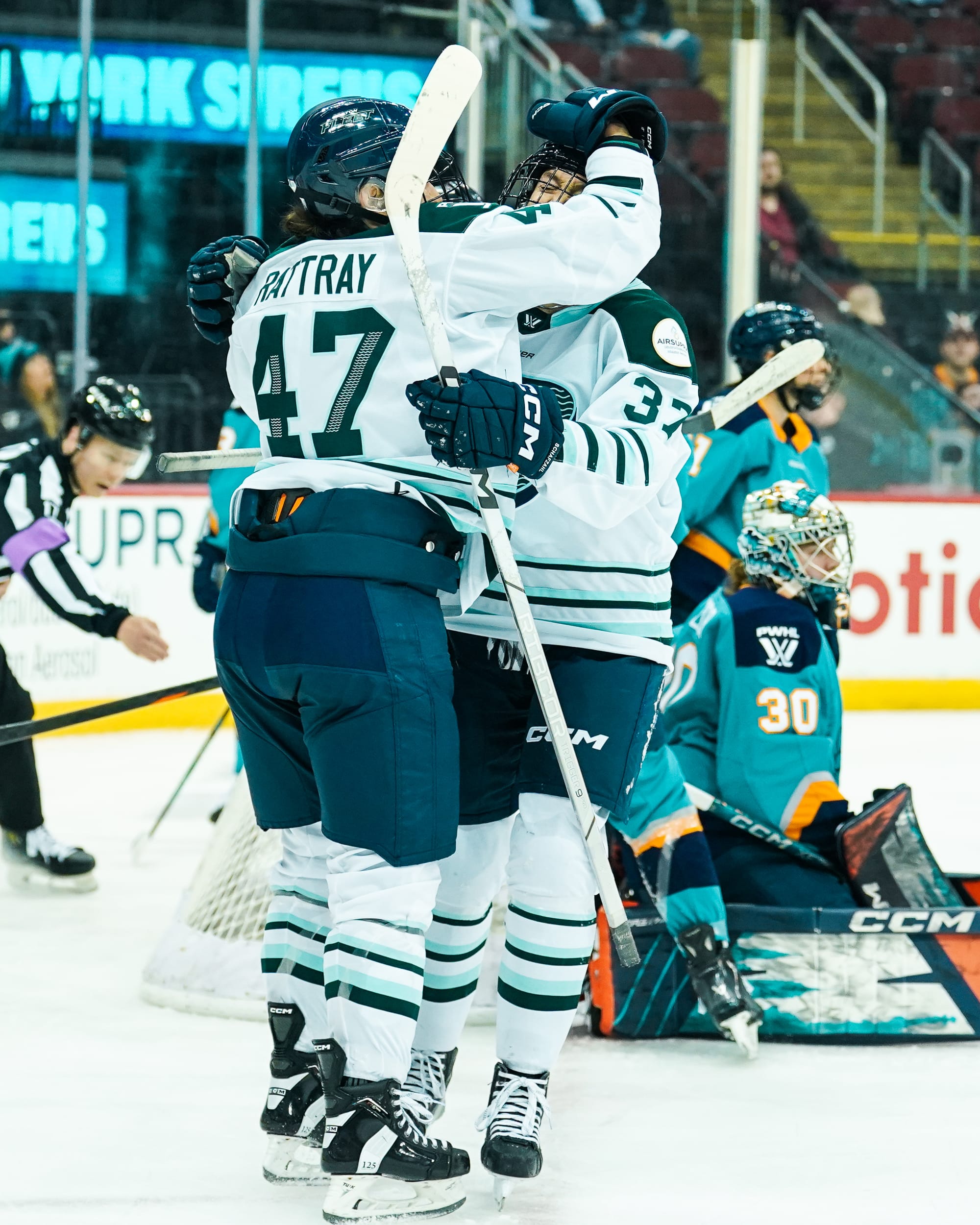 Rattray and Schafzahl celebrate with a hug off to the side of the goal. Rattray is patting Schafzahl on the head. They are wearing white away uniforms.