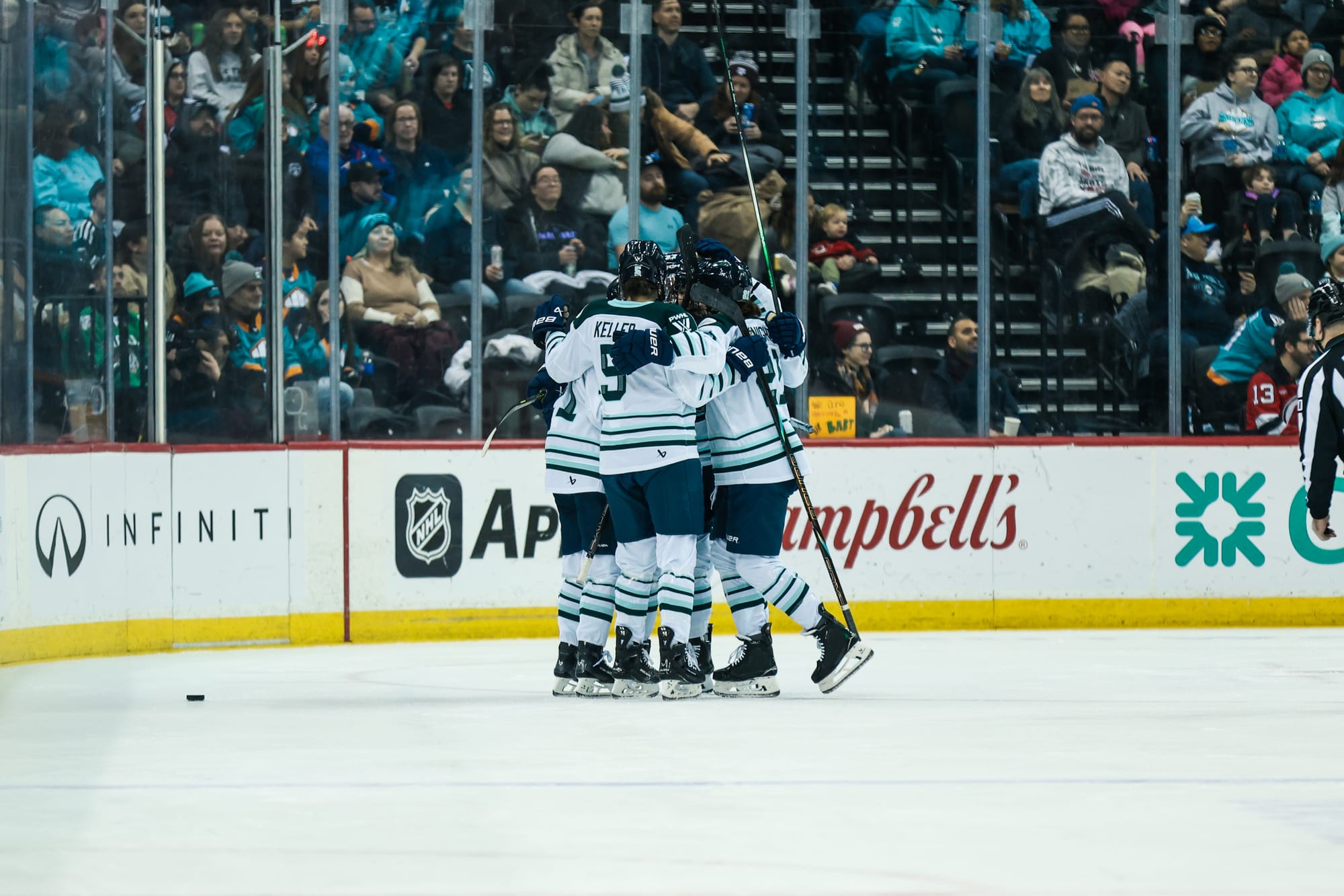 Fleet players celebrate with a tight group hug at the top of one of the circles. They are wearing white away uniforms.