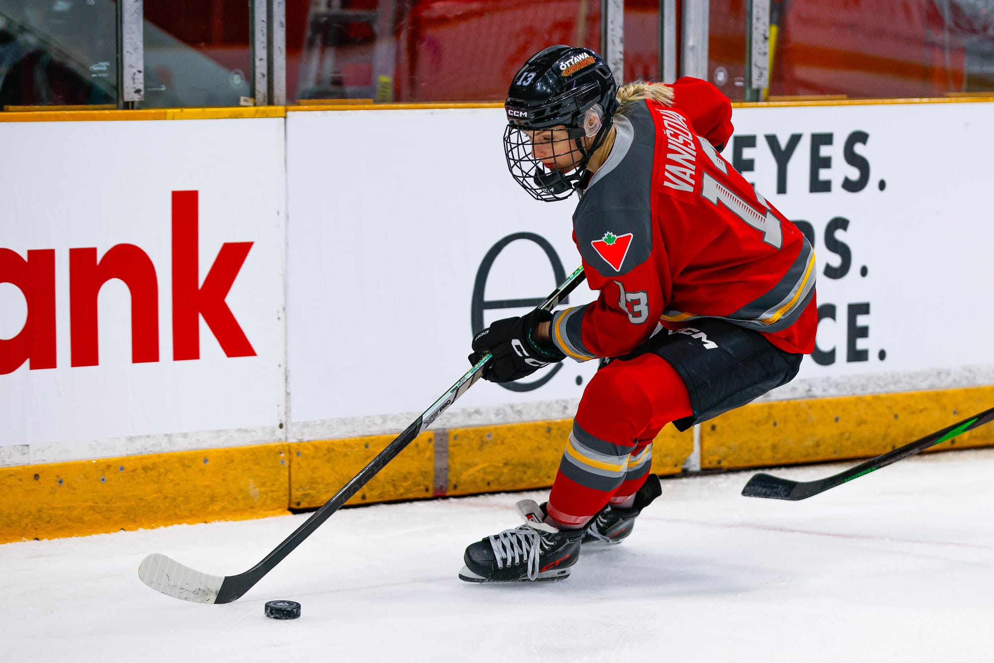 Vanišová looks down at the puck as she skates along the boards. She is wearing a red home uniform.