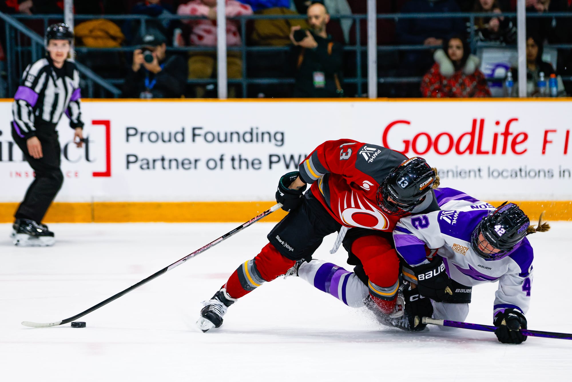 Thomspn (right in whhite) hits the ice as Vanišová (left in red) leans on her. Vanišová is currently in possession of the puck.