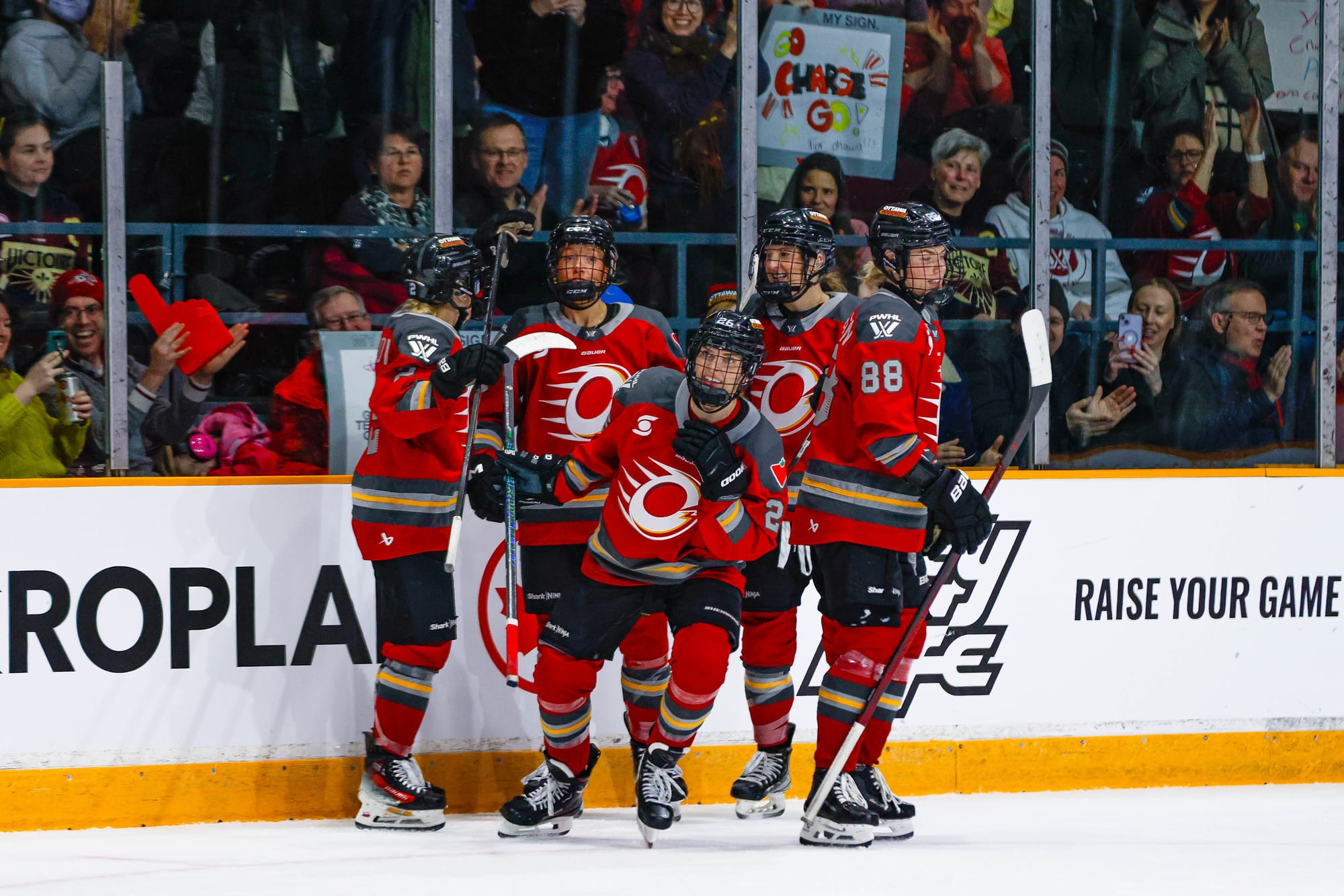 Ottawa Charge players celebrate a goal. They just finished a group hug and are heading to the handshake line at the bench. They are wearing red home uniforms.