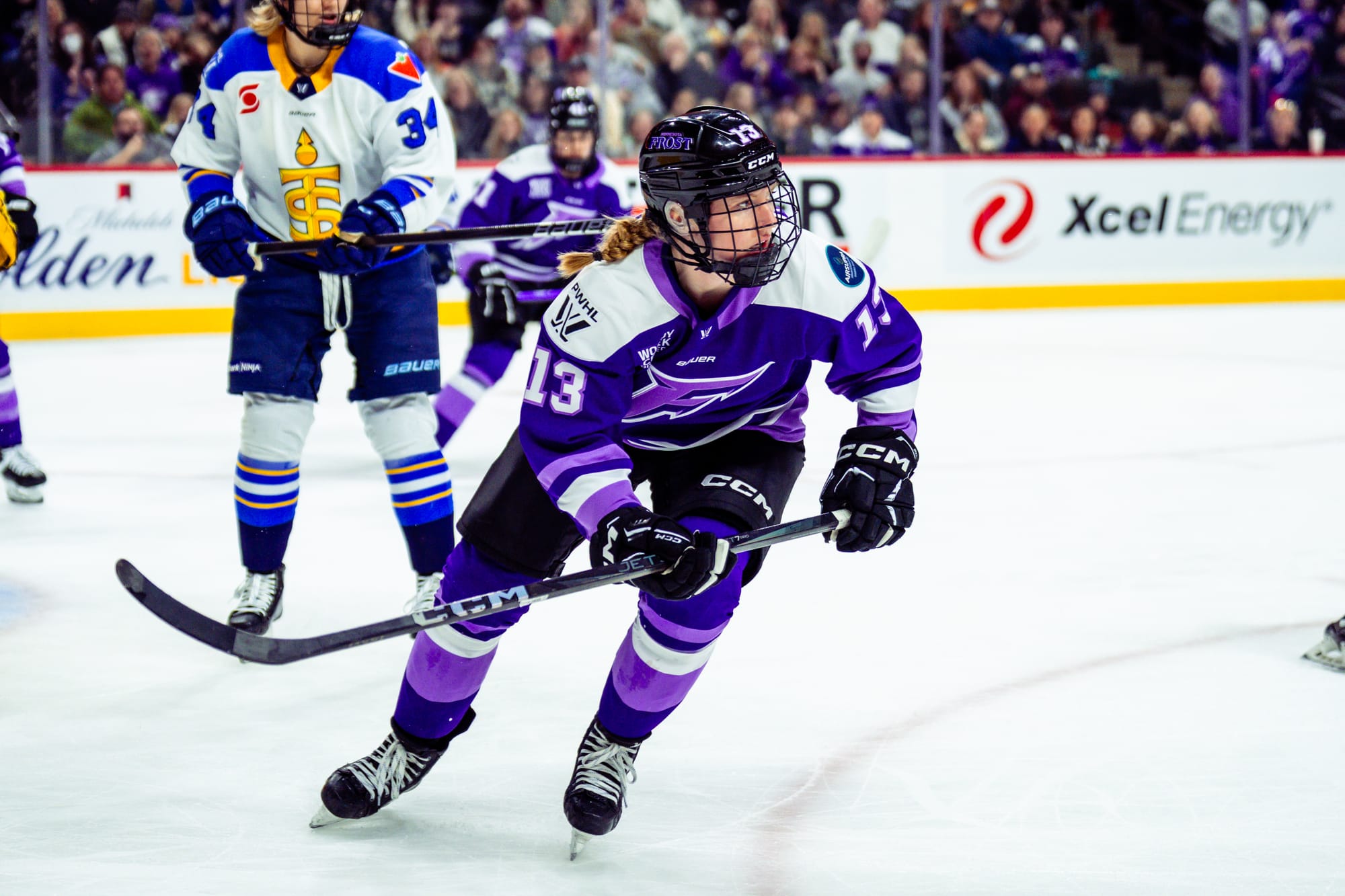 Zumwinkle looks to her left, as she skates with her stick in the air. She is wearing a purple home uniform.