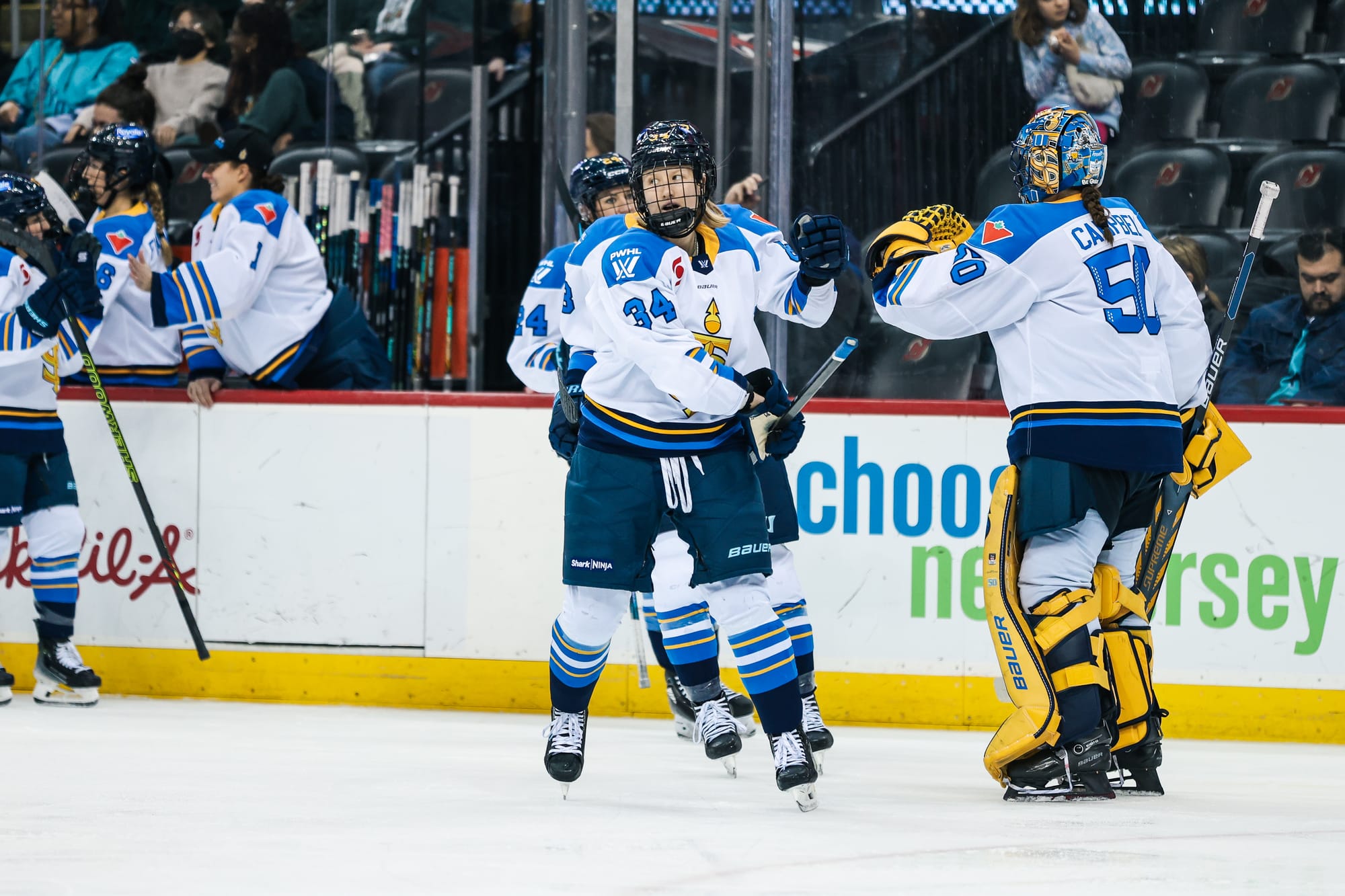 Miller skates toward the camera after fist-bumping Kristen Campbell. She is looking to her right and wearing a white away uniform.