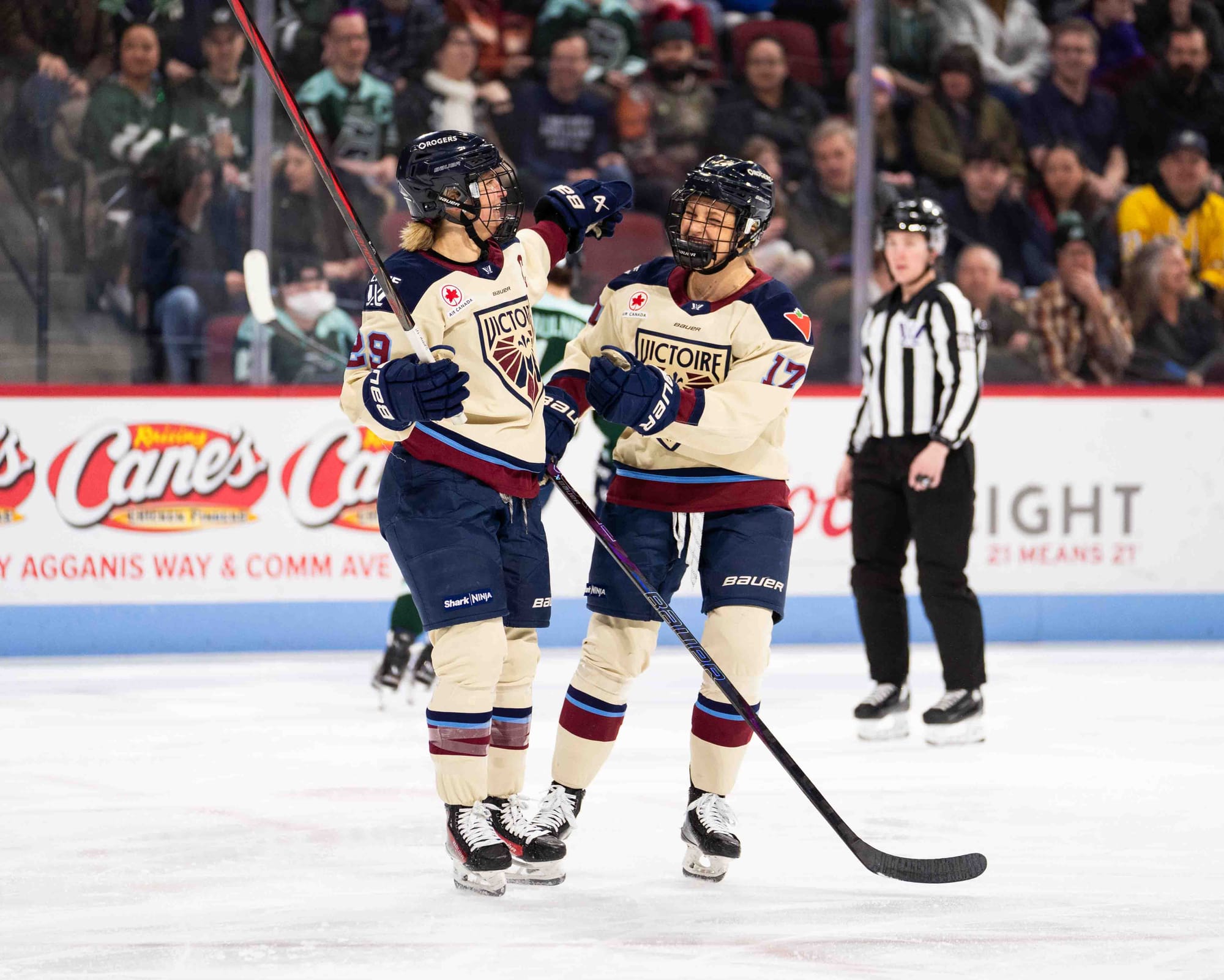 Poulin (left) and Greig (right) smile and hug. They are wearing cream away uniforms.