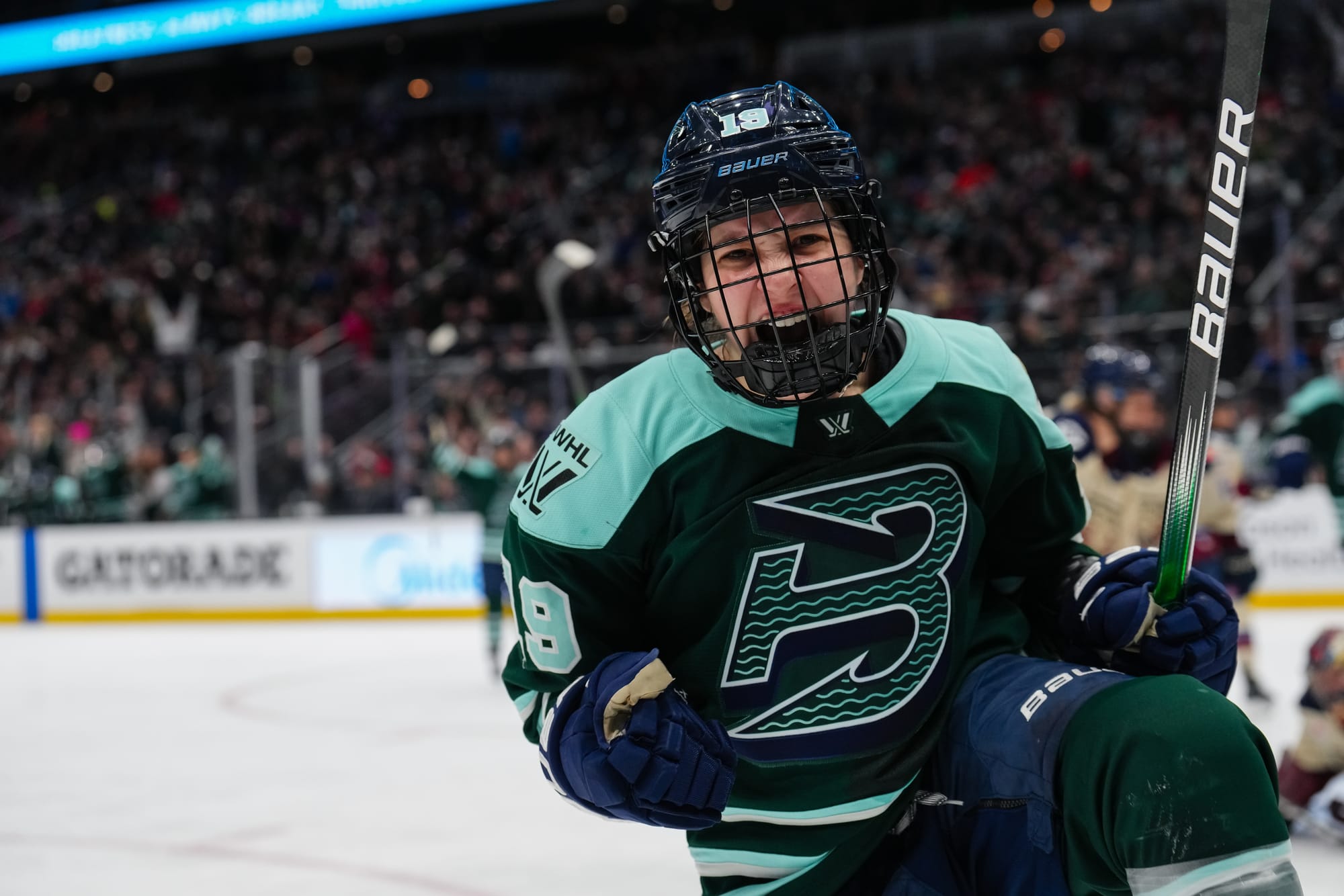 Bilka pumps her firts and yells in celebration. She is facing the camera and wearing a green home uniform.