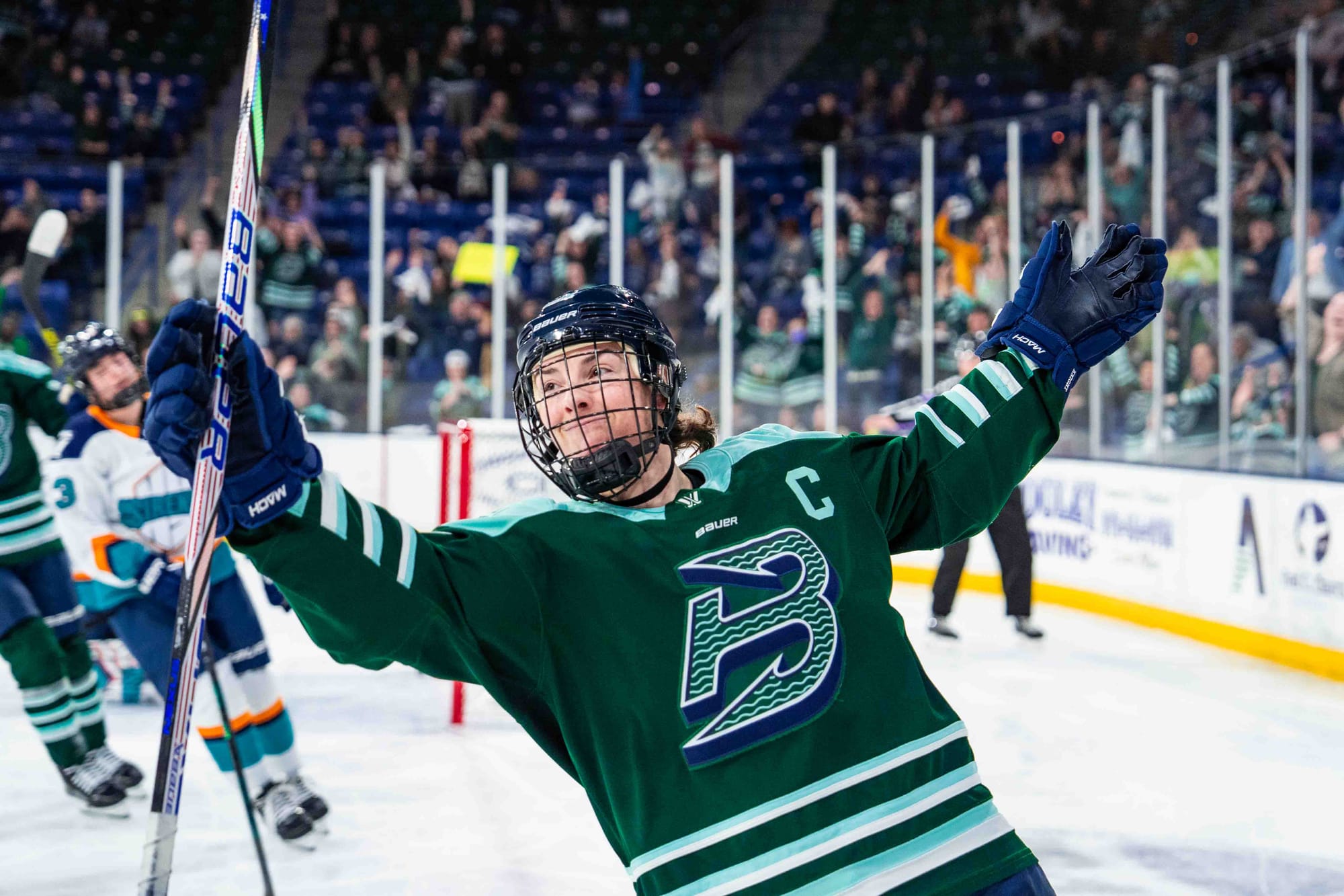 Hilary Knight smiles and raises her arms in celebration. She is facing the camera and wearing a green home uniform.