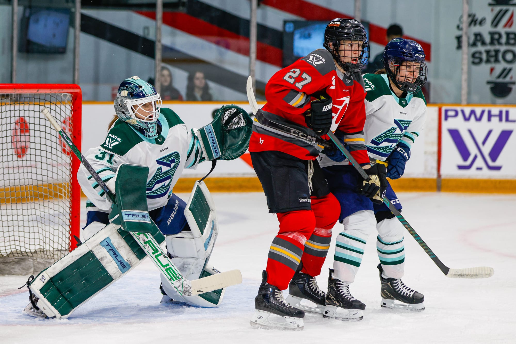 Frankel peers around Sidney Morin and Shiann Darkangelo player who are standing in front of her as she attempts to track a play happening out of frame. Frankel and Morin are wearing white away uniforms, while Darkangelo is in red.